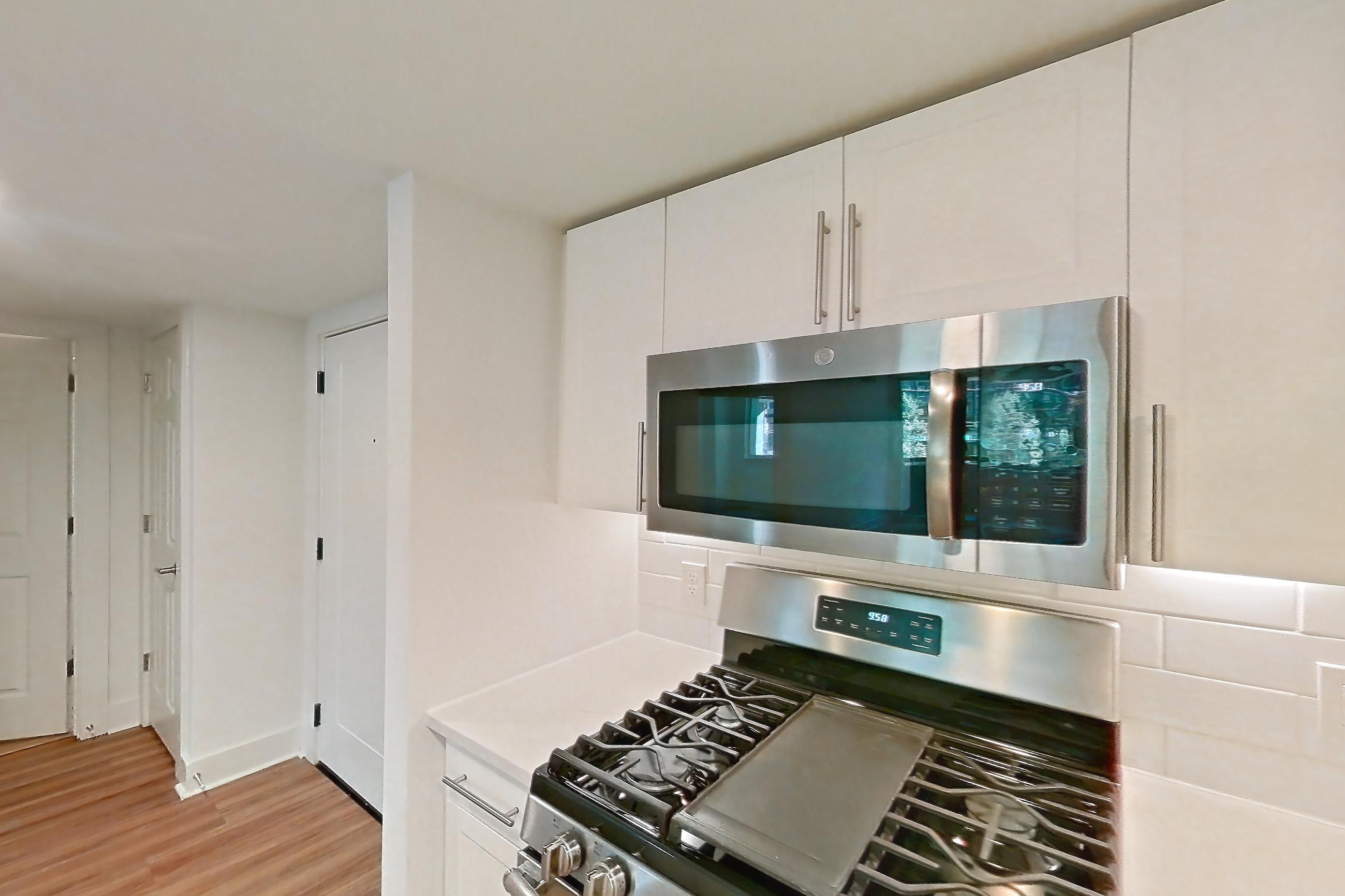 Kitchen with dishwasher, gas range, light countertops, light stone countertops, light wood-finish flooring, microwave, oven/range, refrigerator, and stainless steel appliances, Apartment 01-0208 at Cortland Pentagon City
