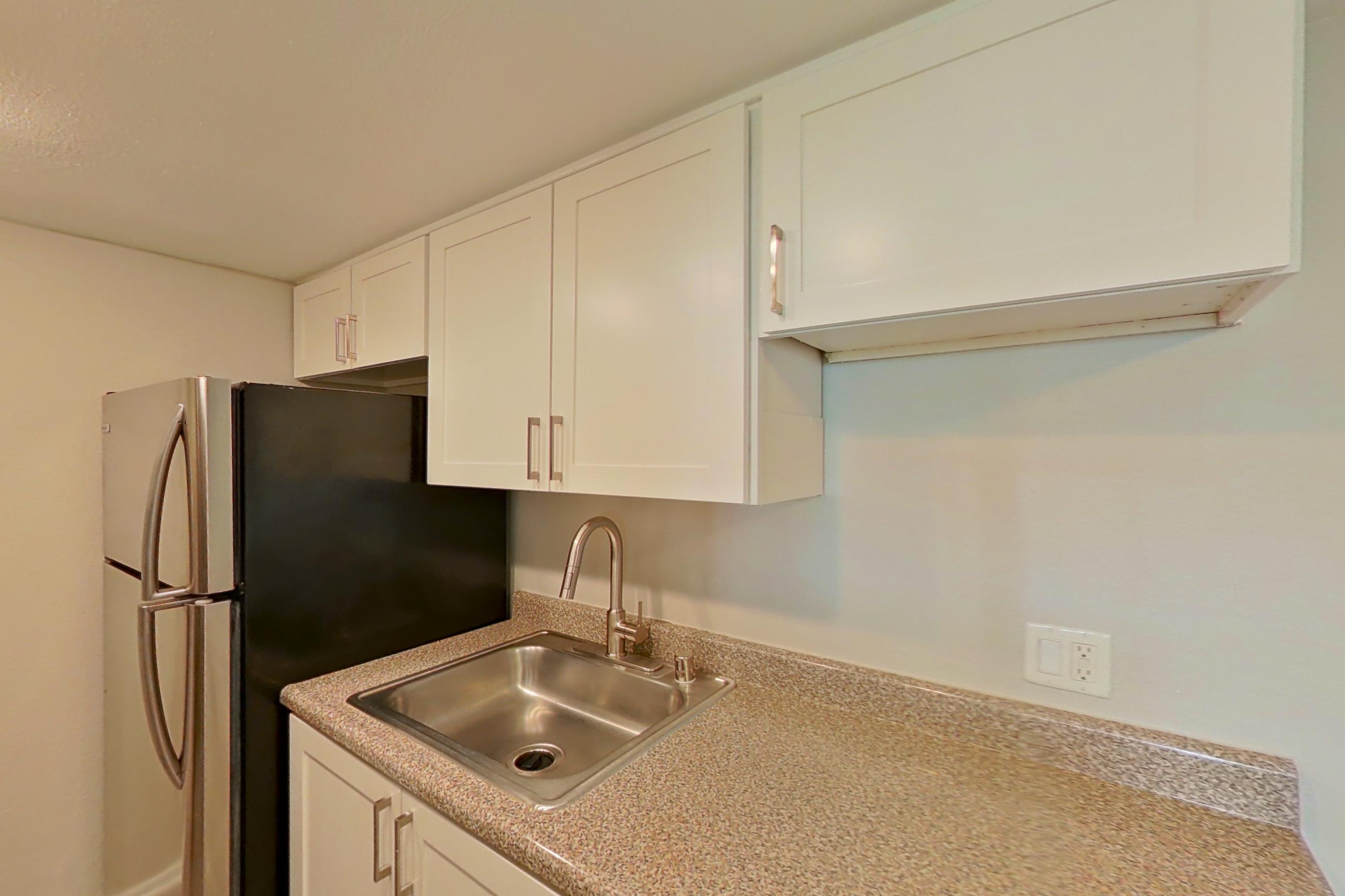Kitchen with black appliances, dishwasher, electric range, light countertops, light wood-finish flooring, oven/range, and stainless steel appliances, Apartment 12 at Avana Rancho Cucamonga