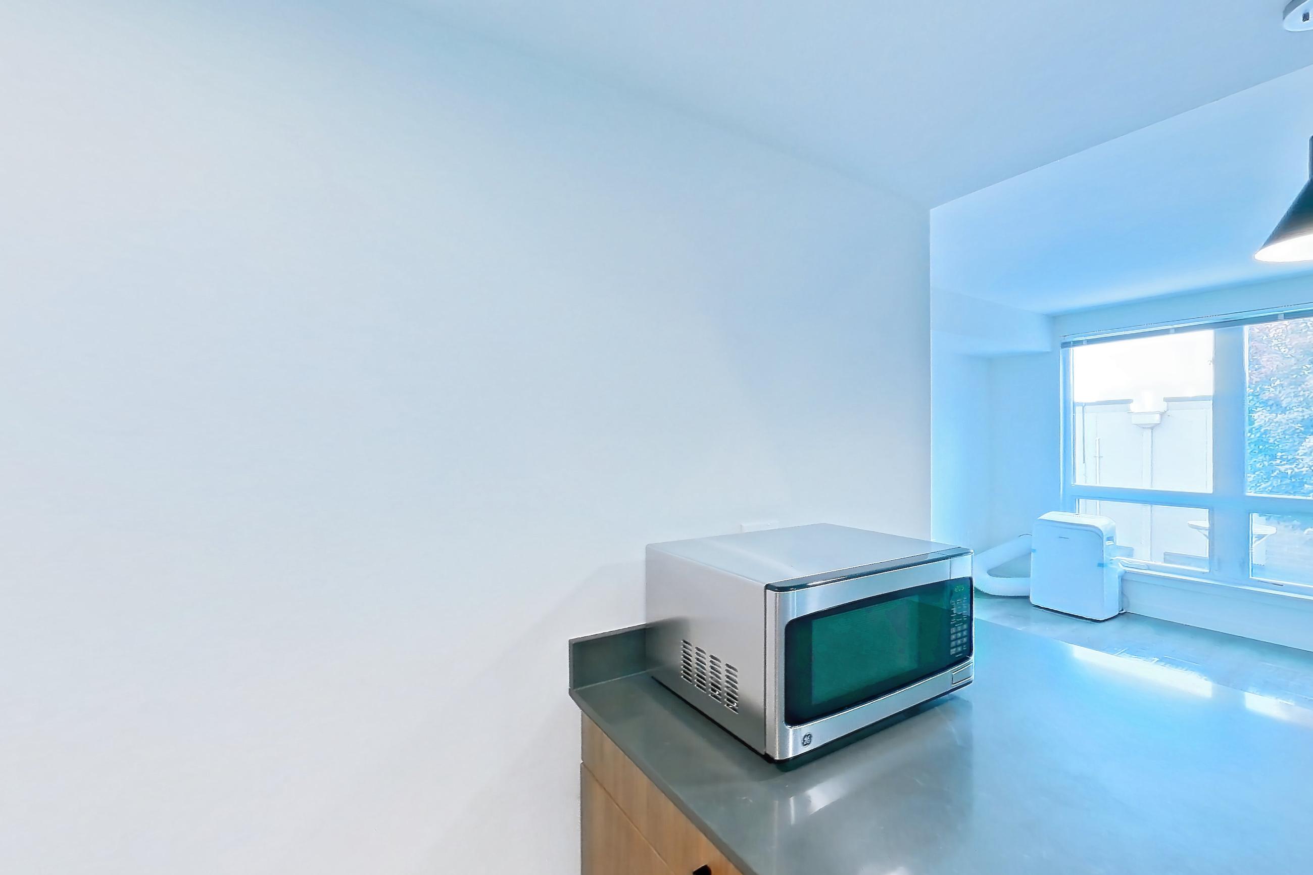 Kitchen with dark countertops, dark wood-finish flooring, dishwasher, electric range, light countertops, light wood-finish flooring, microwave, oven/range, range hood, refrigerator, and stainless steel appliances, Apartment 201 at Talisman