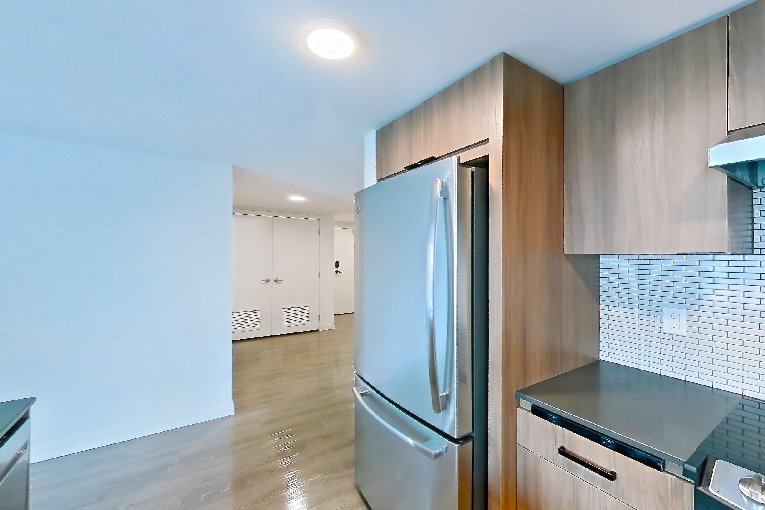 Kitchen with dark countertops, dark wood-finish flooring, dishwasher, electric range, light countertops, light wood-finish flooring, microwave, oven/range, range hood, refrigerator, and stainless steel appliances, Apartment 201 at Talisman