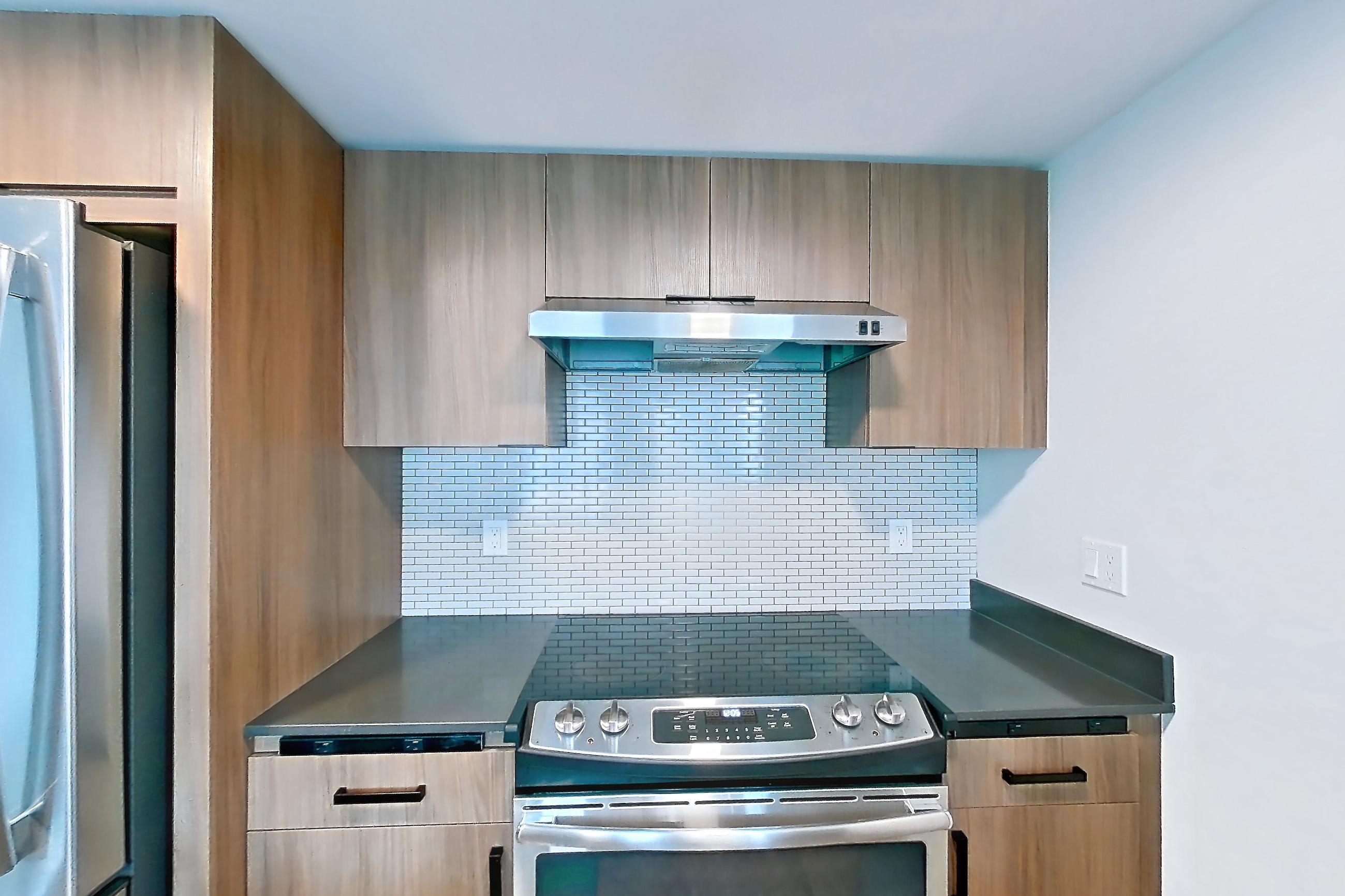 Kitchen with dark countertops, dark wood-finish flooring, dishwasher, electric range, light countertops, light wood-finish flooring, microwave, oven/range, range hood, refrigerator, and stainless steel appliances, Apartment 201 at Talisman