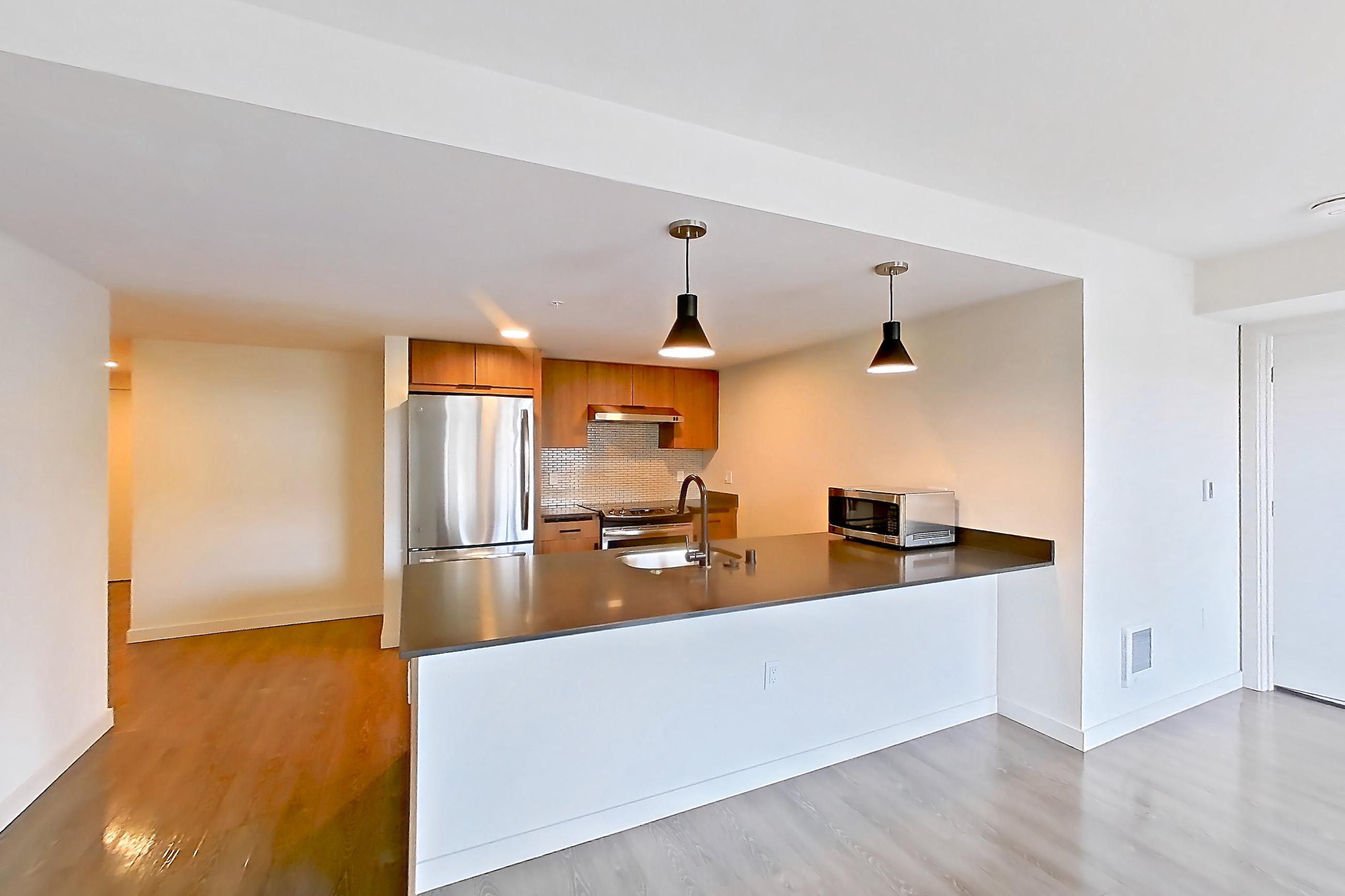 Living room with dark countertops, dark wood-finish flooring, electric range, light countertops, light wood-finish flooring, microwave, oven/range, refrigerator, and stainless steel appliances, Apartment 201 at Talisman