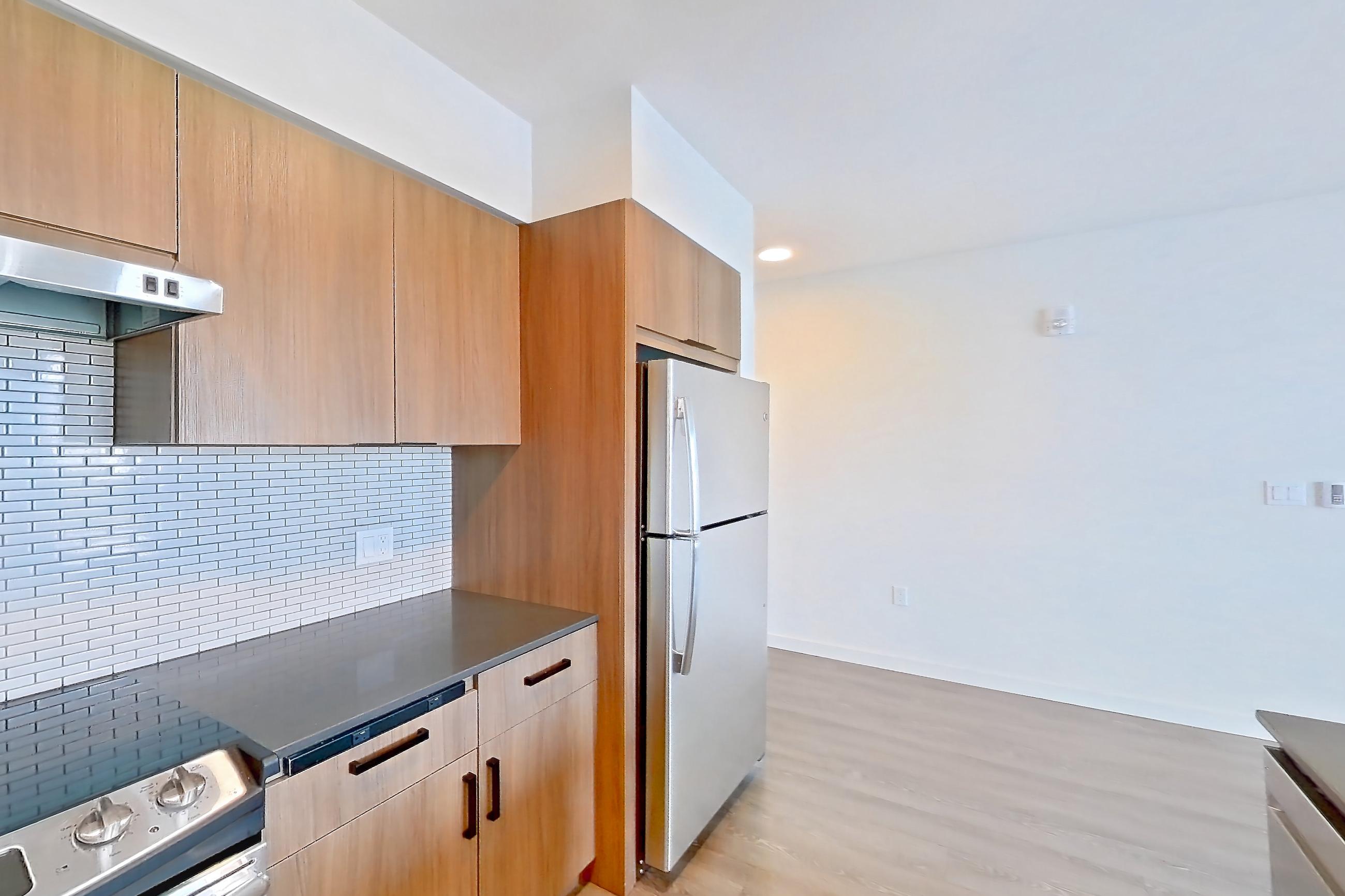 Kitchen with dark countertops, dishwasher, electric range, light countertops, light wood-finish flooring, microwave, oven/range, range hood, refrigerator, stainless steel appliances, and white appliances, Apartment 440 at Talisman