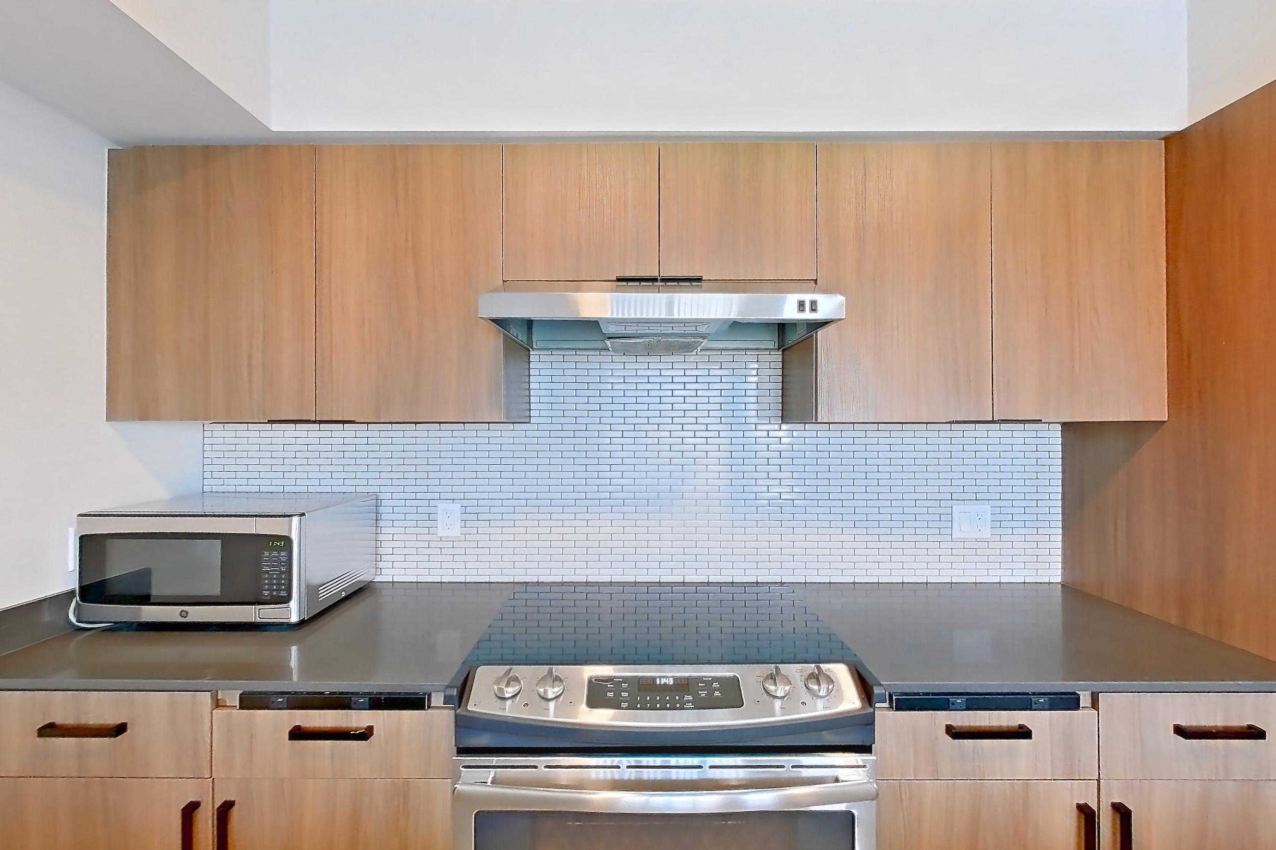 Kitchen with dark countertops, dishwasher, electric range, light countertops, light wood-finish flooring, microwave, oven/range, range hood, refrigerator, stainless steel appliances, and white appliances, Apartment 440 at Talisman