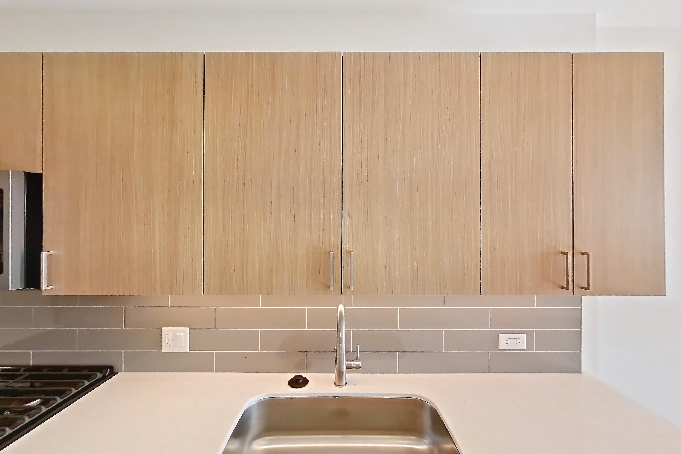Kitchen with black appliances, dishwasher, gas range, light countertops, light stone countertops, light wood-finish flooring, microwave, oven/range, refrigerator, and stainless steel appliances, Apartment 816 at One Oak Brook Commons