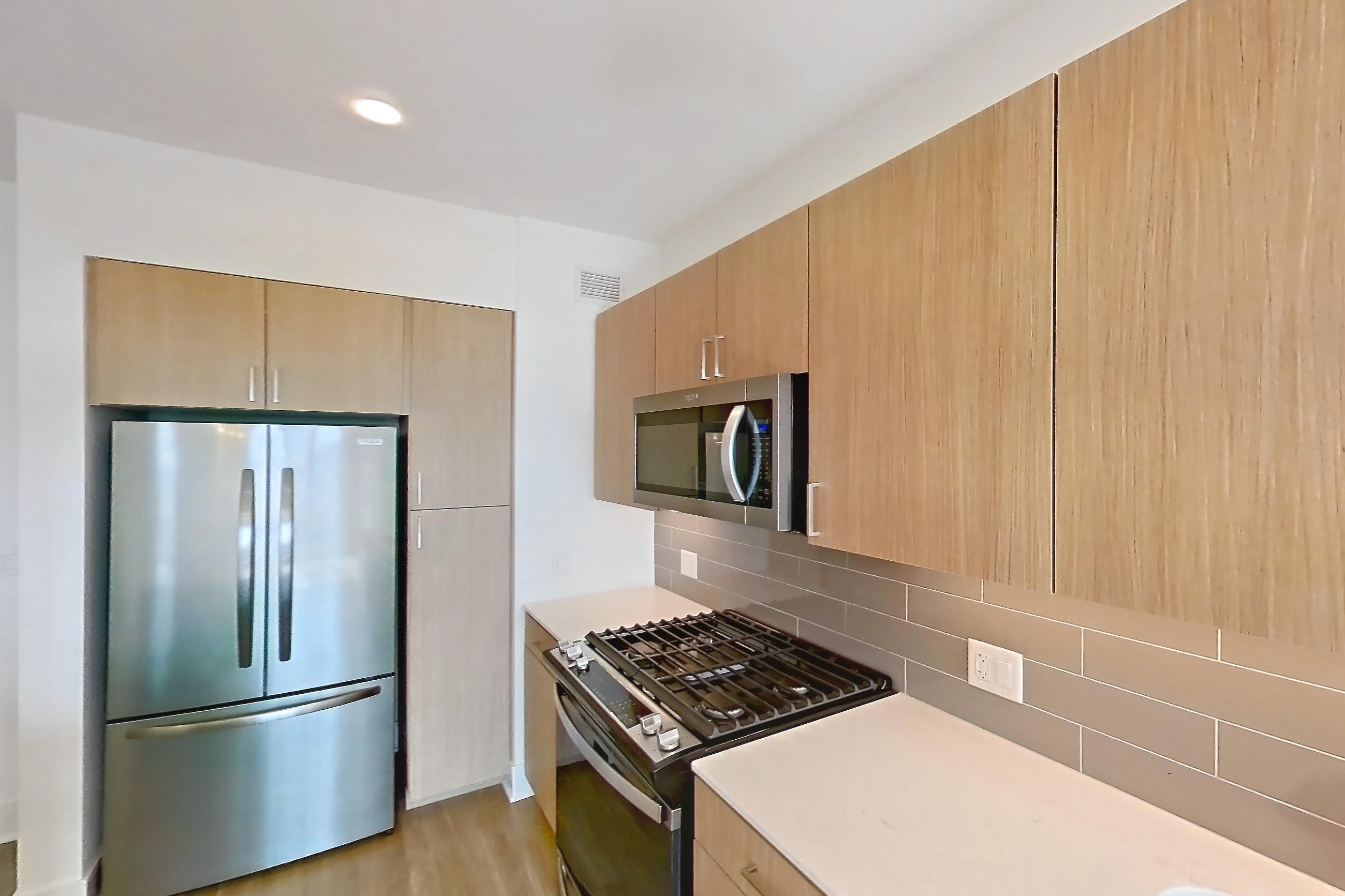 Kitchen with black appliances, dishwasher, gas range, light countertops, light stone countertops, light wood-finish flooring, microwave, oven/range, refrigerator, and stainless steel appliances, Apartment 816 at One Oak Brook Commons