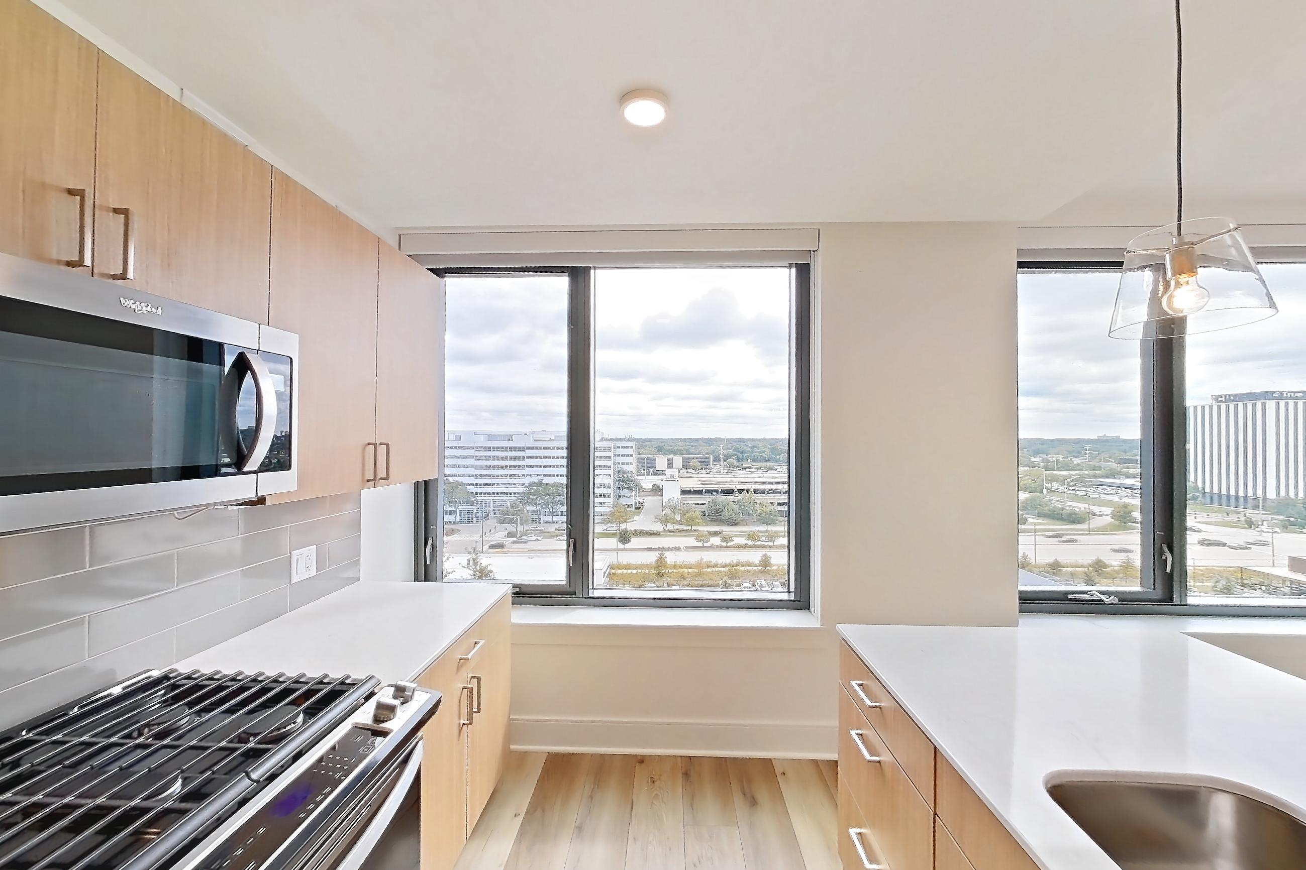 Kitchen with dishwasher, gas range, light stone countertops, light wood-finish flooring, oven/range, and stainless steel appliances, Apartment 1020 at One Oak Brook Commons