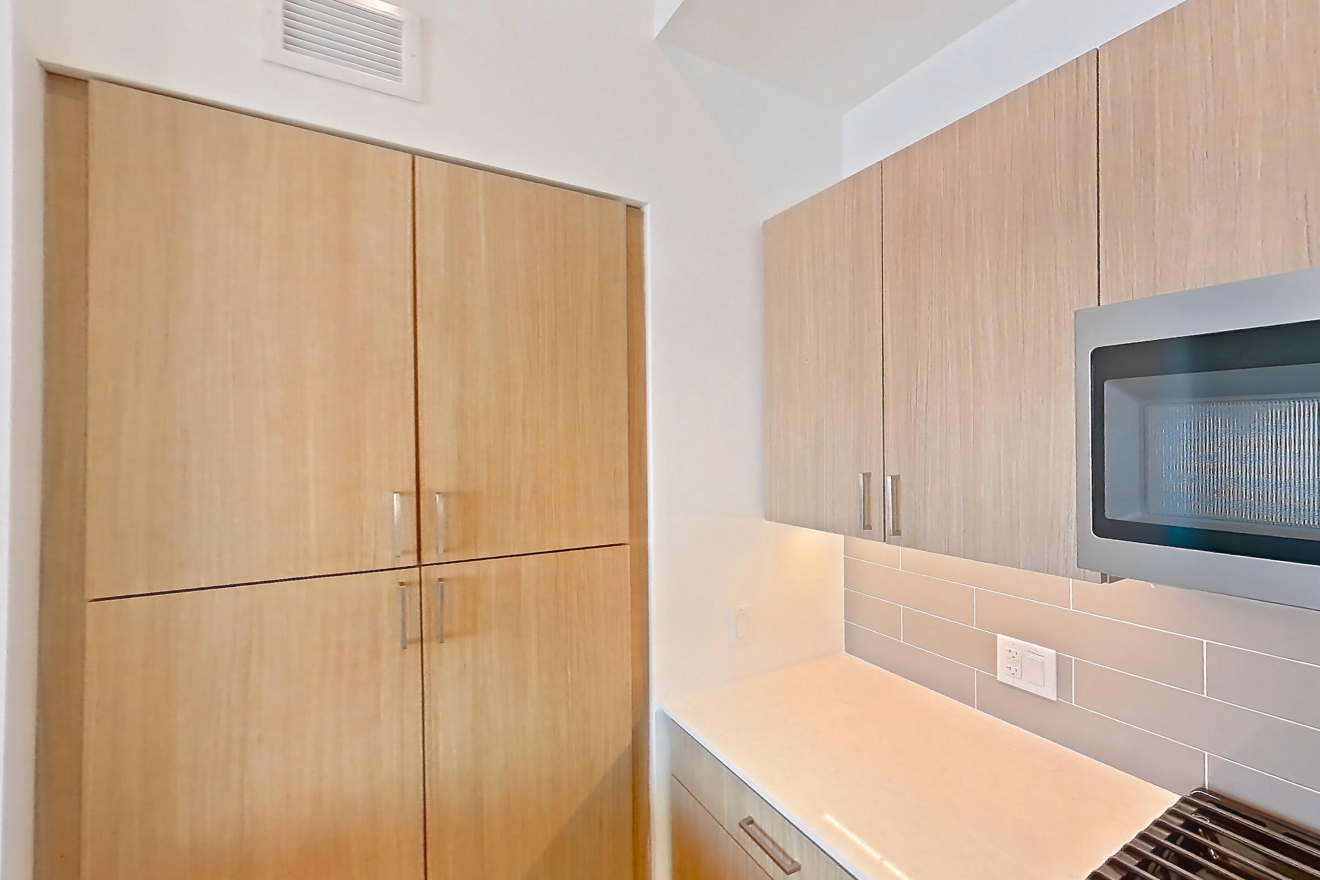Kitchen with dishwasher, gas range, kitchen island, light countertops, light stone countertops, light wood-finish flooring, oven/range, refrigerator, and stainless steel appliances, Apartment 1612 at One Oak Brook Commons
