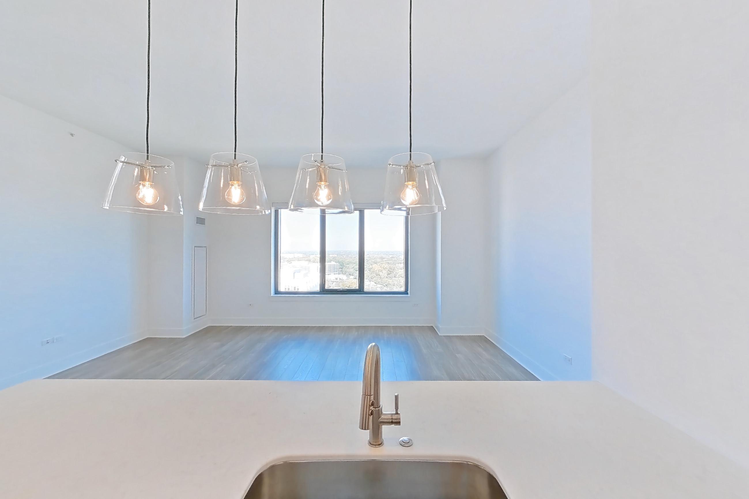 Kitchen with dishwasher, gas range, kitchen island, light countertops, light stone countertops, light wood-finish flooring, oven/range, refrigerator, and stainless steel appliances, Apartment 1612 at One Oak Brook Commons