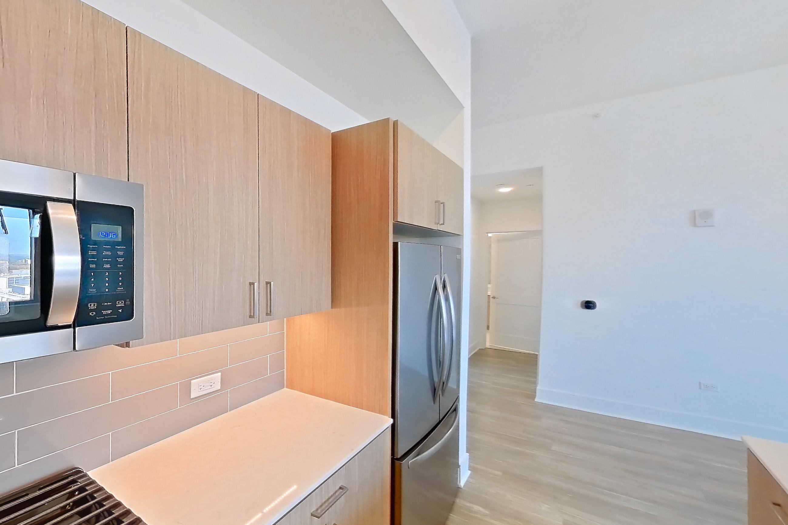 Kitchen with dishwasher, gas range, kitchen island, light countertops, light stone countertops, light wood-finish flooring, oven/range, refrigerator, and stainless steel appliances, Apartment 1612 at One Oak Brook Commons