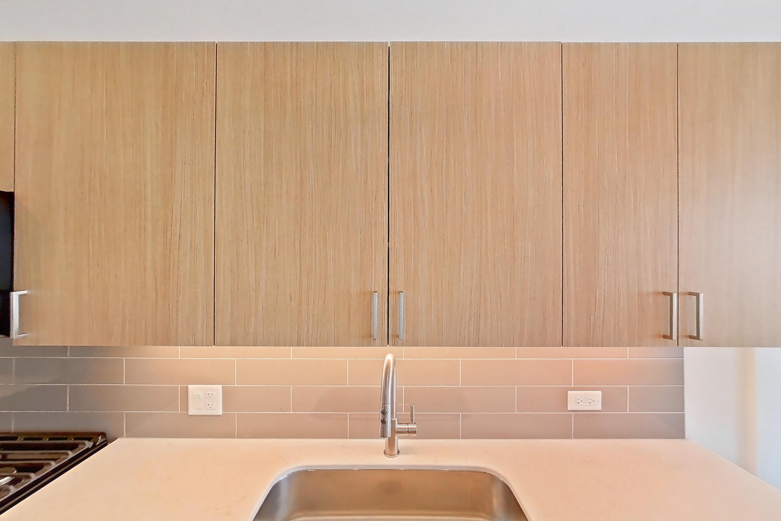 Kitchen with black appliances, dishwasher, gas range, light countertops, light stone countertops, light wood-finish flooring, microwave, oven/range, refrigerator, and stainless steel appliances, Apartment 1102 at One Oak Brook Commons