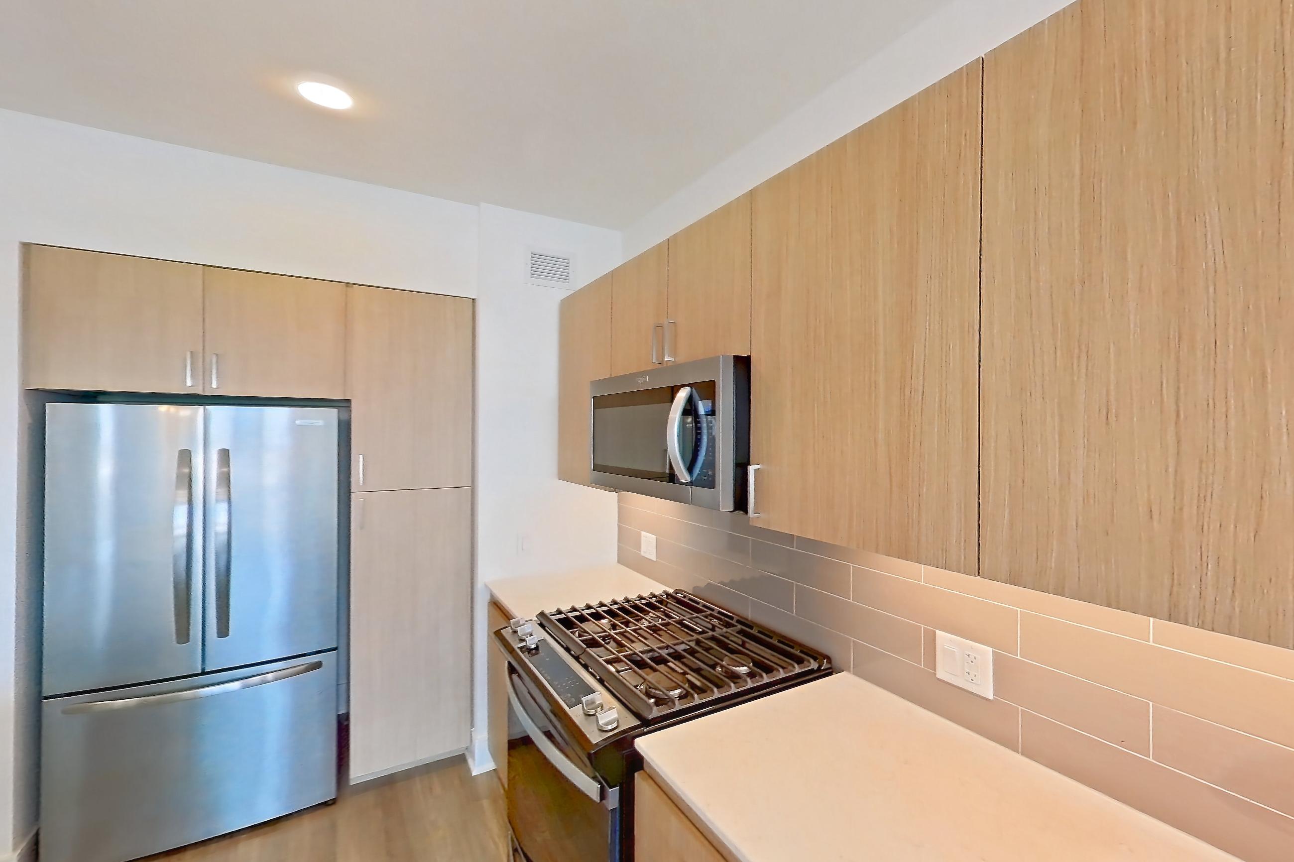 Kitchen with black appliances, dishwasher, gas range, light countertops, light stone countertops, light wood-finish flooring, microwave, oven/range, refrigerator, and stainless steel appliances, Apartment 1102 at One Oak Brook Commons