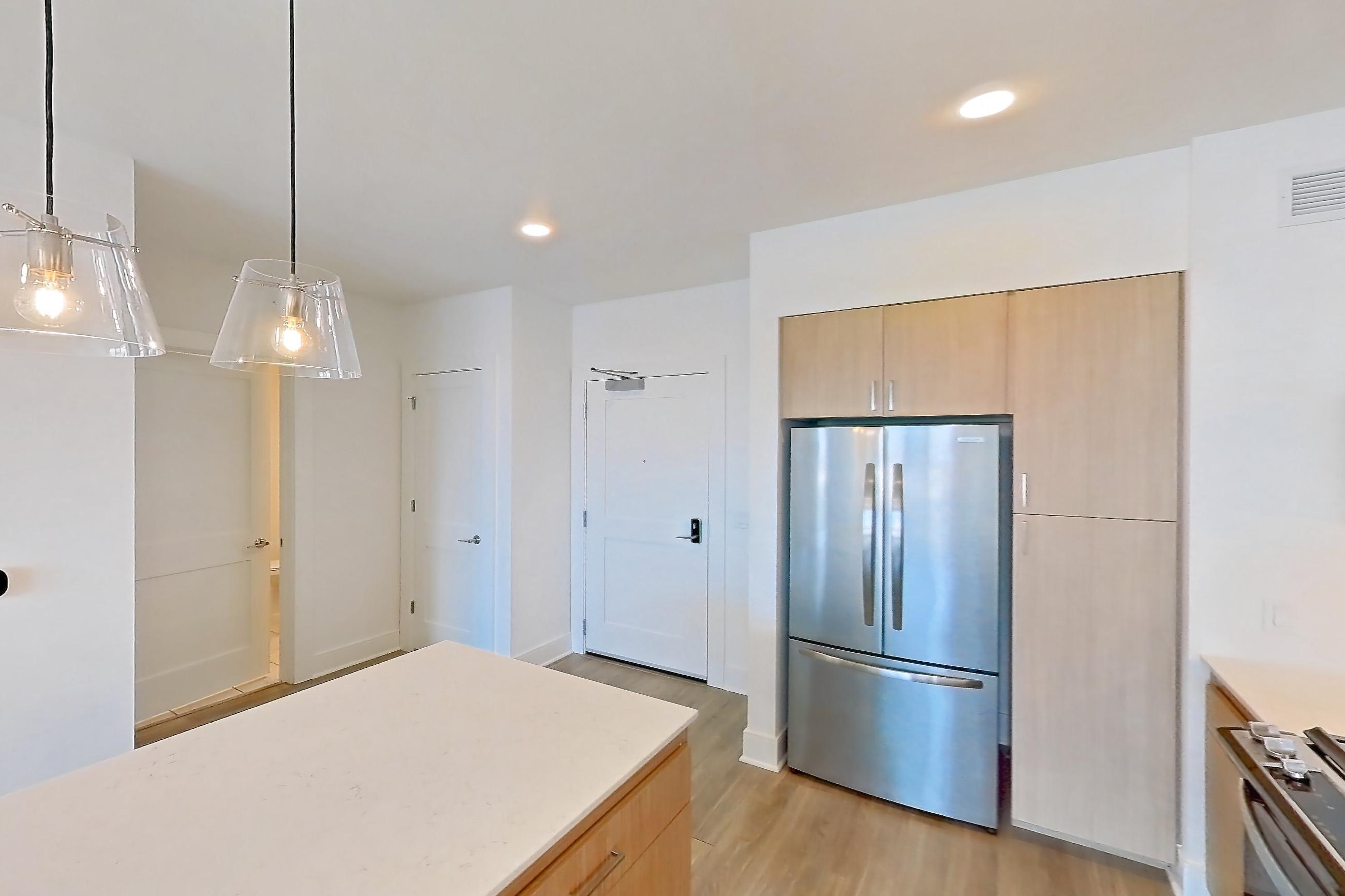 Kitchen with black appliances, dishwasher, gas range, light countertops, light stone countertops, light wood-finish flooring, microwave, oven/range, refrigerator, and stainless steel appliances, Apartment 1102 at One Oak Brook Commons