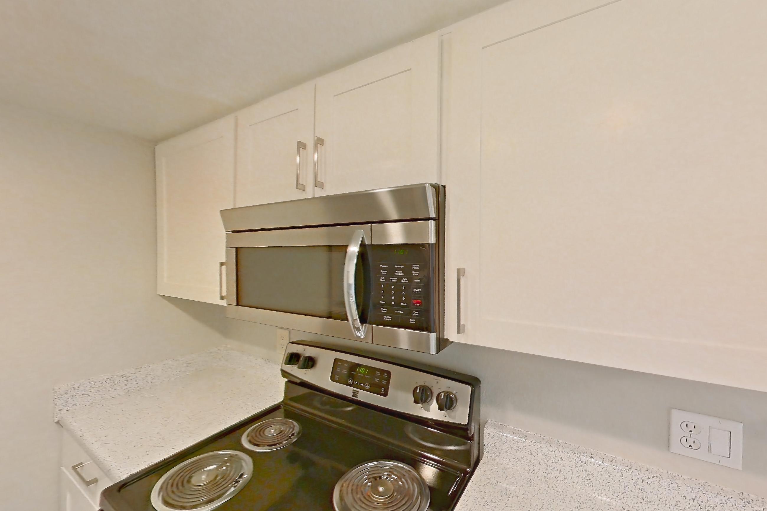 Kitchen with black appliances, dishwasher, electric range, light countertops, light stone countertops, light wood-finish flooring, microwave, oven/range, and stainless steel appliances, Apartment 01 at Avana Rancho Cucamonga