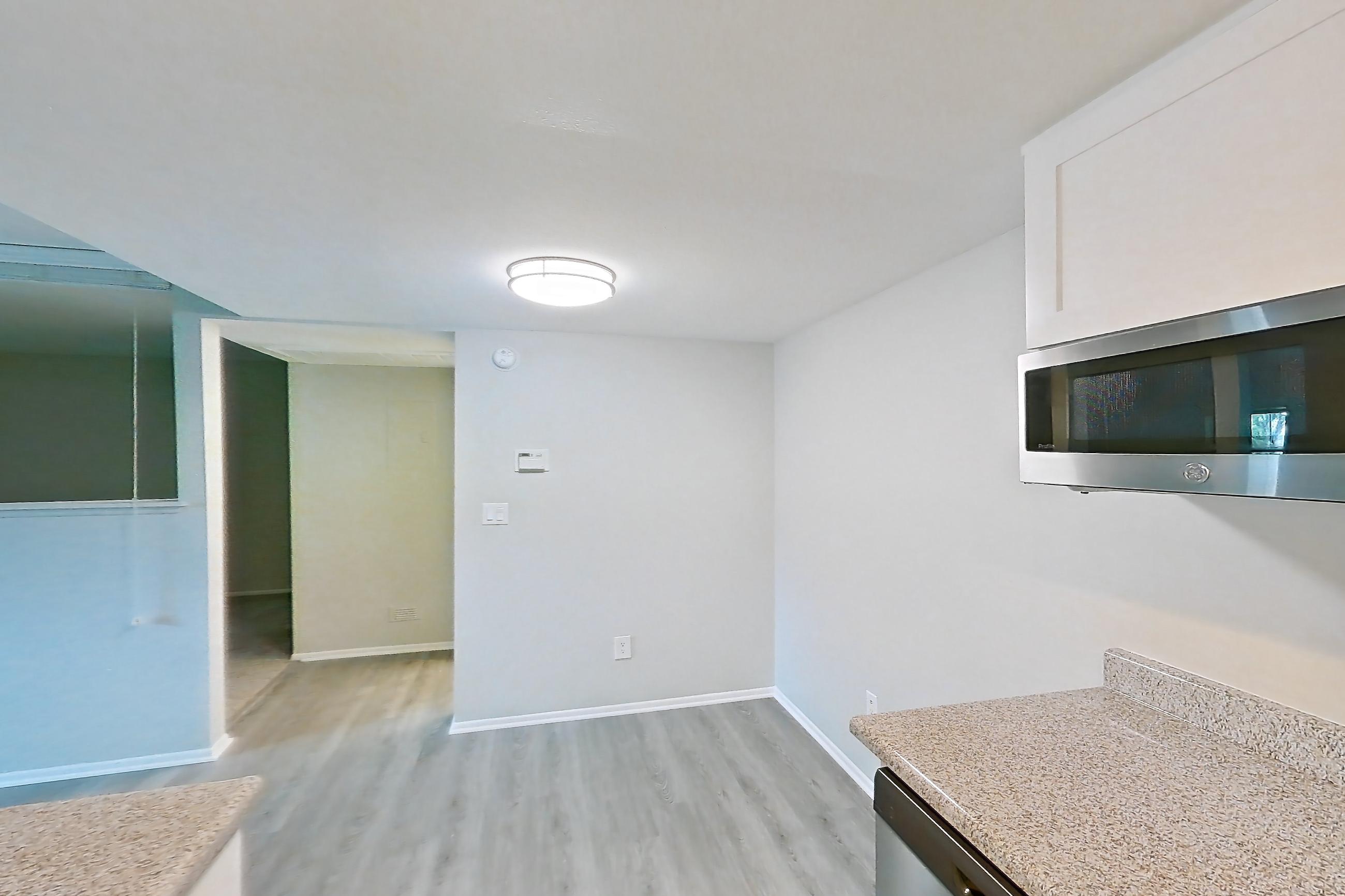 Kitchen with black appliances, dishwasher, electric range, light countertops, light stone countertops, light wood-finish flooring, oven/range, refrigerator, and stainless steel appliances, Apartment 02 at Avana Rancho Cucamonga