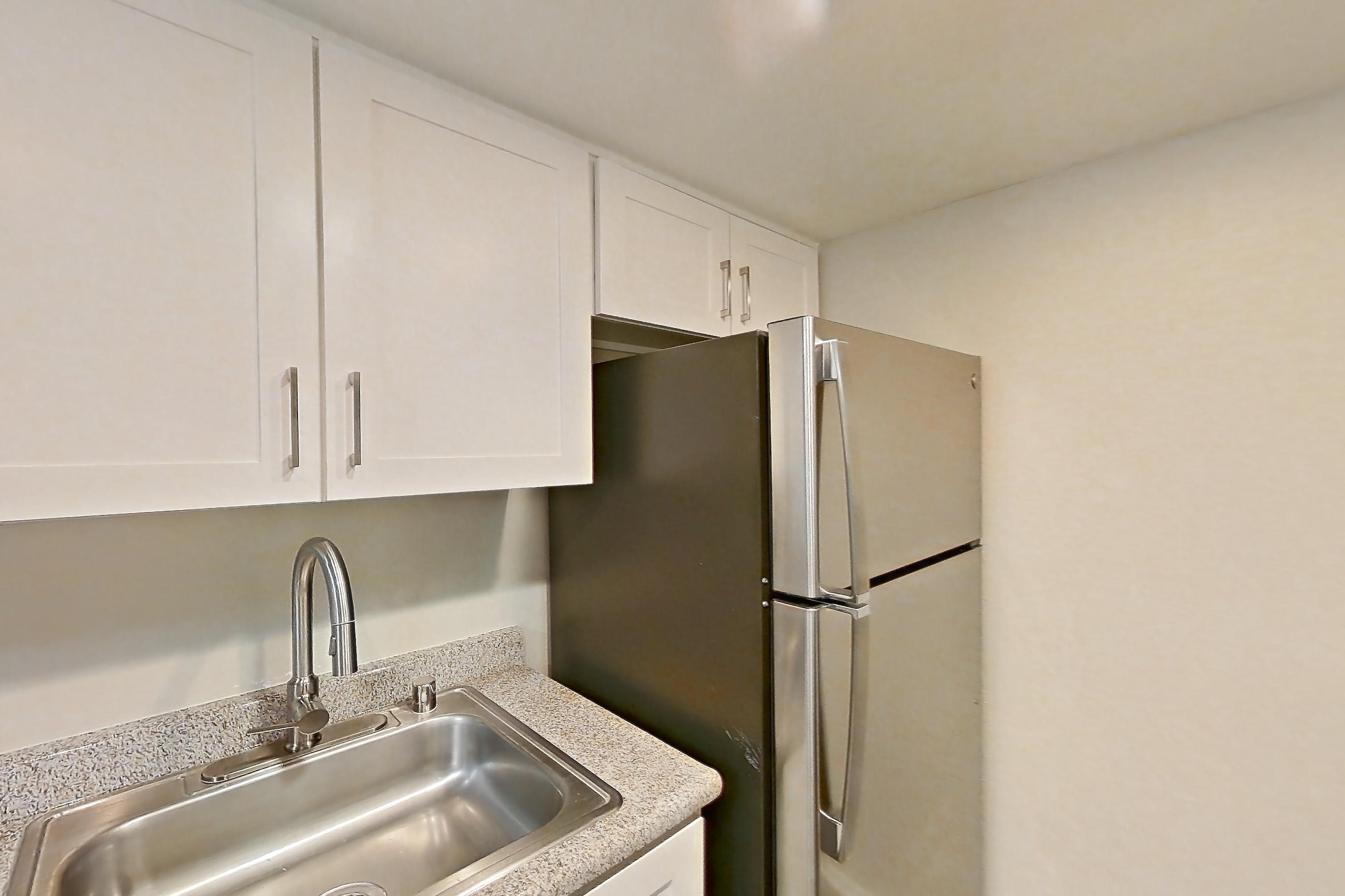 Kitchen with black appliances, dishwasher, electric range, light countertops, light stone countertops, light wood-finish flooring, oven/range, refrigerator, and stainless steel appliances, Apartment 02 at Avana Rancho Cucamonga