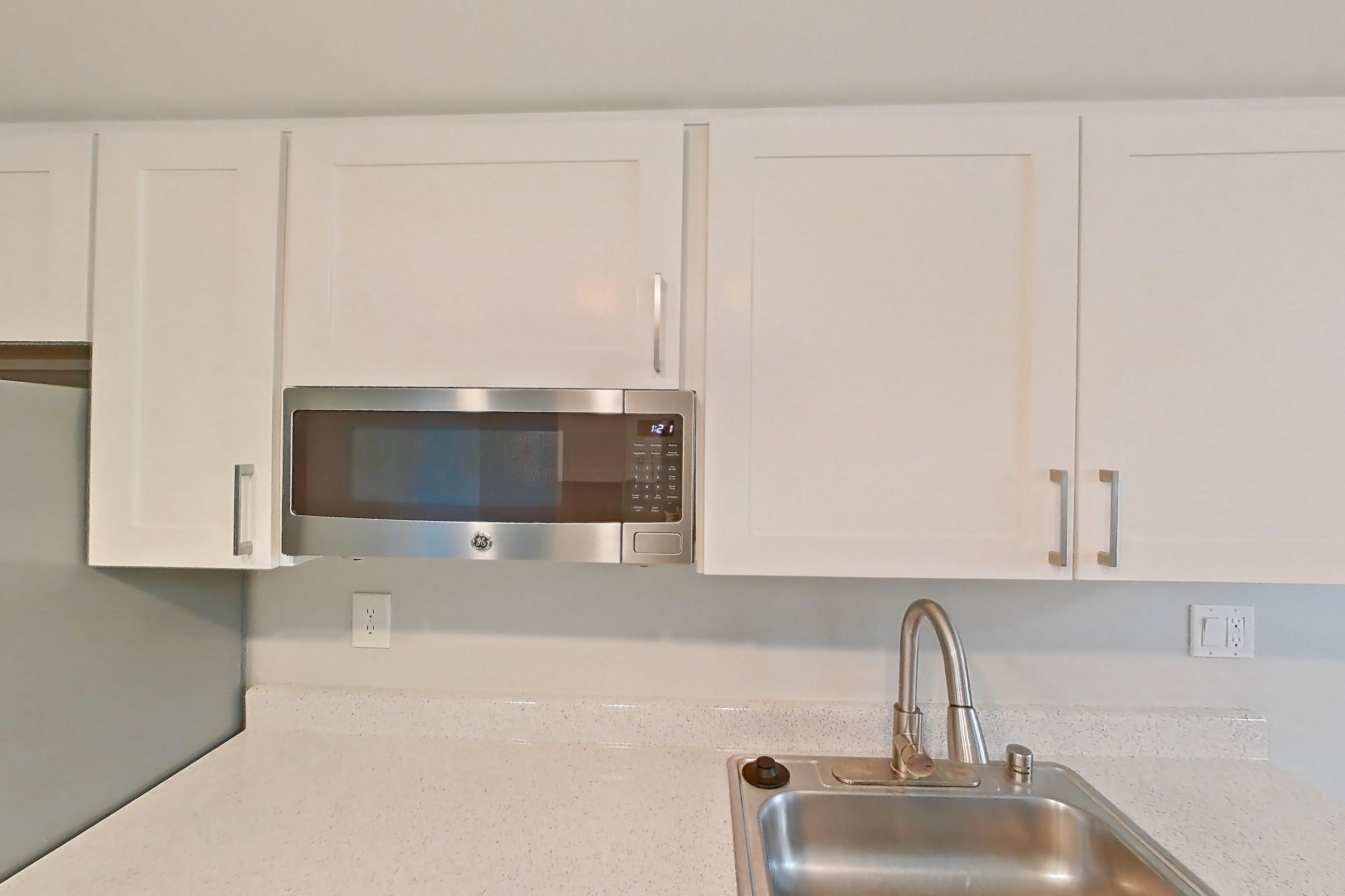 Kitchen with dark wood-finish flooring, dishwasher, light countertops, light stone countertops, light wood-finish flooring, microwave, oven/range, refrigerator, stainless steel appliances, and white appliances, Apartment 03 at Avana Rancho Cucamonga