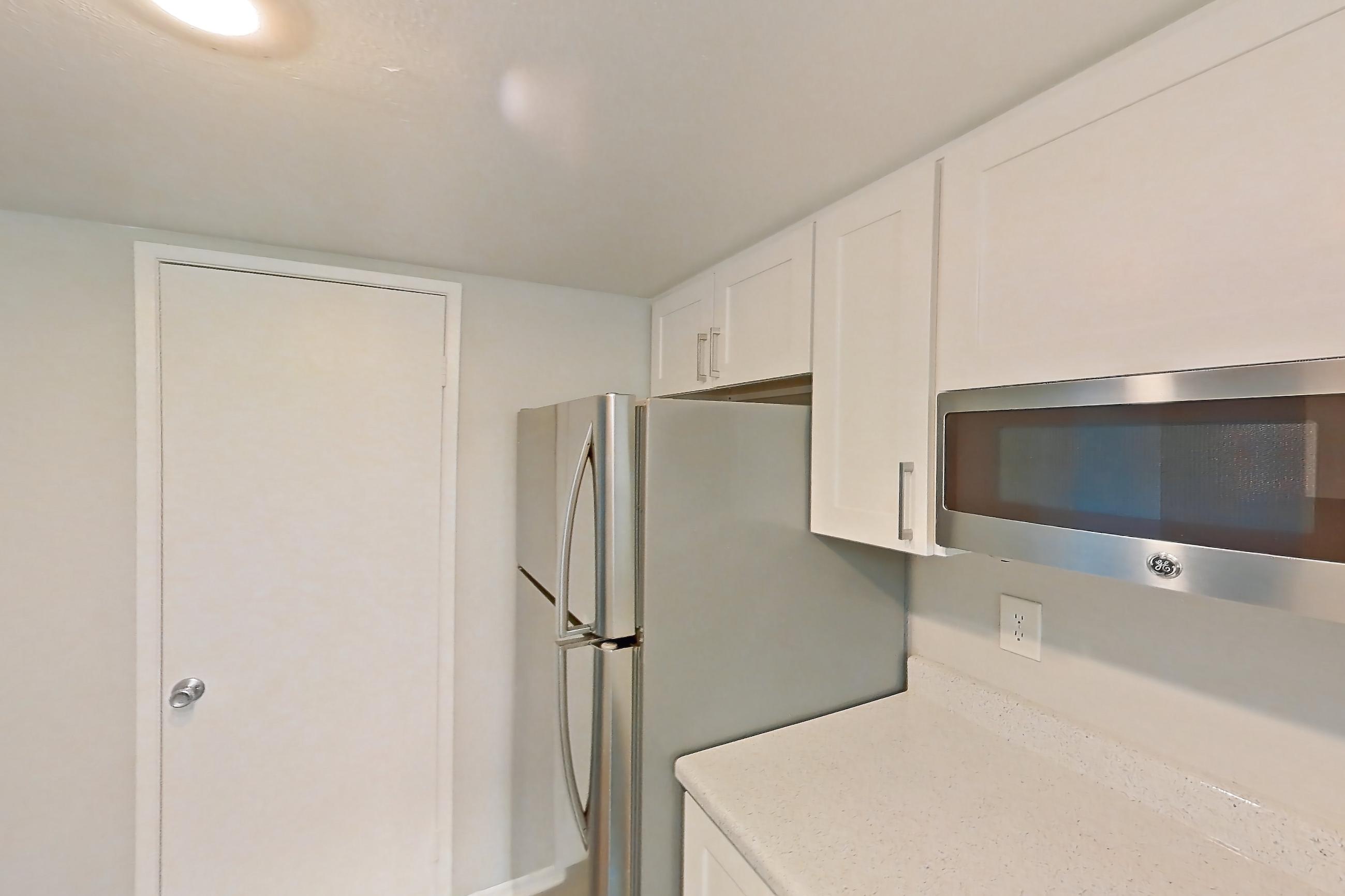 Kitchen with dark wood-finish flooring, dishwasher, light countertops, light stone countertops, light wood-finish flooring, microwave, oven/range, refrigerator, stainless steel appliances, and white appliances, Apartment 03 at Avana Rancho Cucamonga