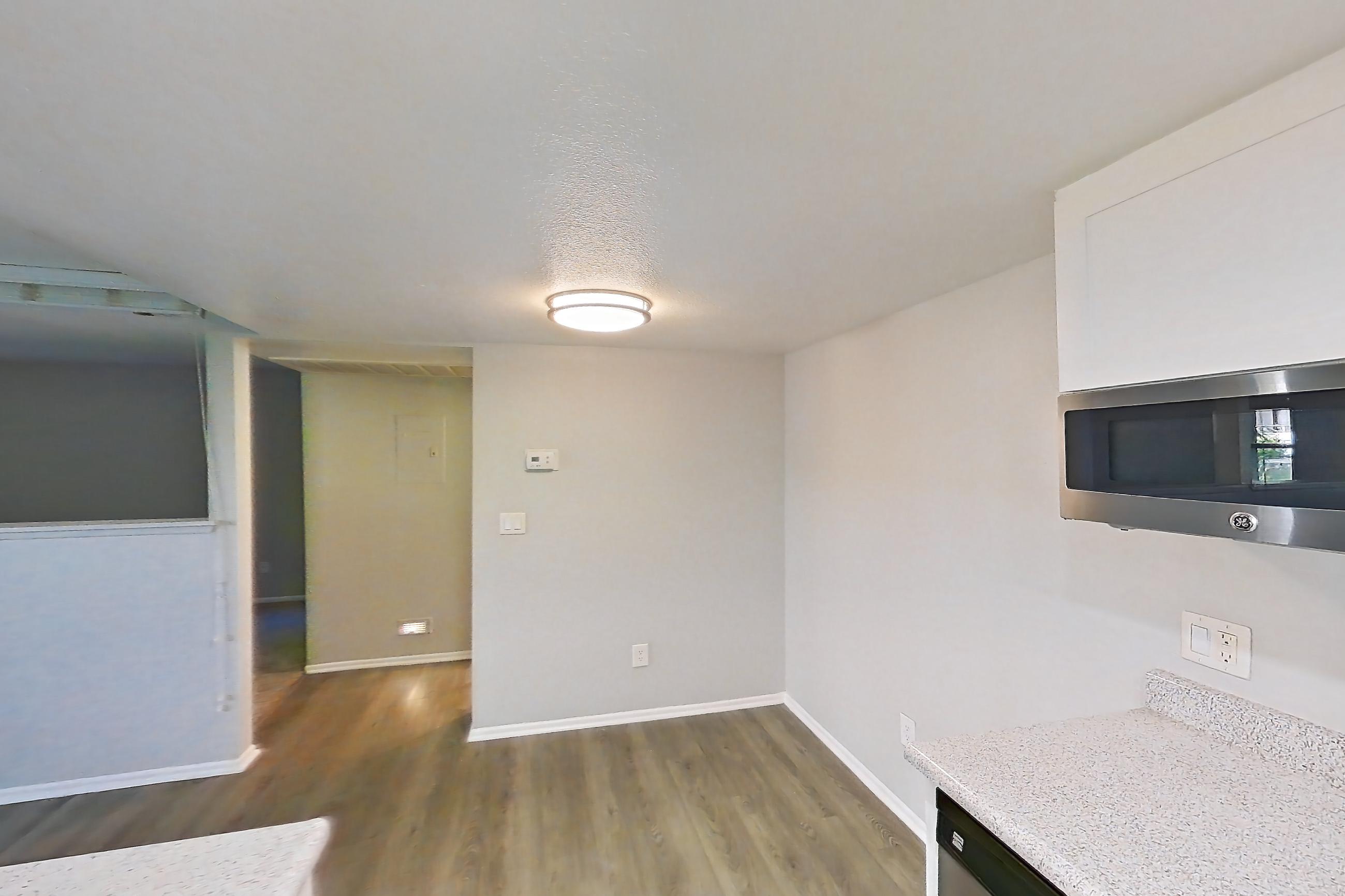 Kitchen with black appliances, dark wood-finish flooring, dishwasher, electric range, light countertops, light stone countertops, light wood-finish flooring, oven/range, range hood, refrigerator, and stainless steel appliances, Apartment 10 at Avana Rancho Cucamonga
