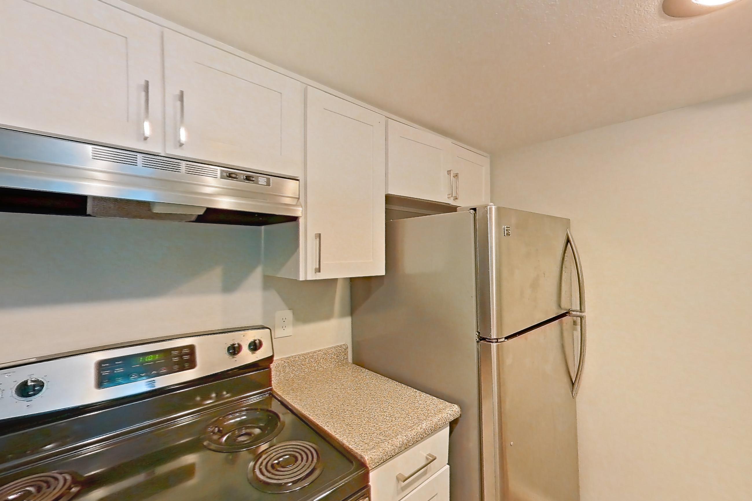 Kitchen with dishwasher, electric range, light countertops, light stone countertops, light wood-finish flooring, oven/range, range hood, and stainless steel appliances, Apartment 01 at Avana Rancho Cucamonga