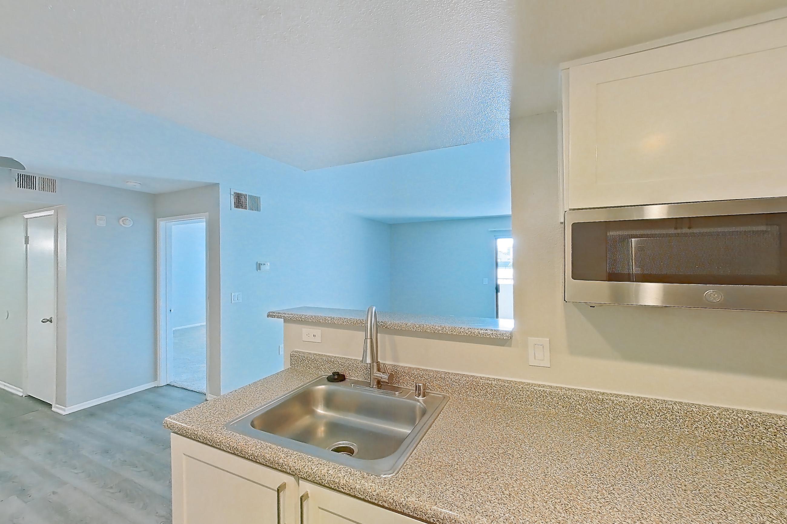 Kitchen with dishwasher, electric range, light countertops, light stone countertops, light wood-finish flooring, oven/range, range hood, refrigerator, and stainless steel appliances, Apartment 23 at Avana Rancho Cucamonga