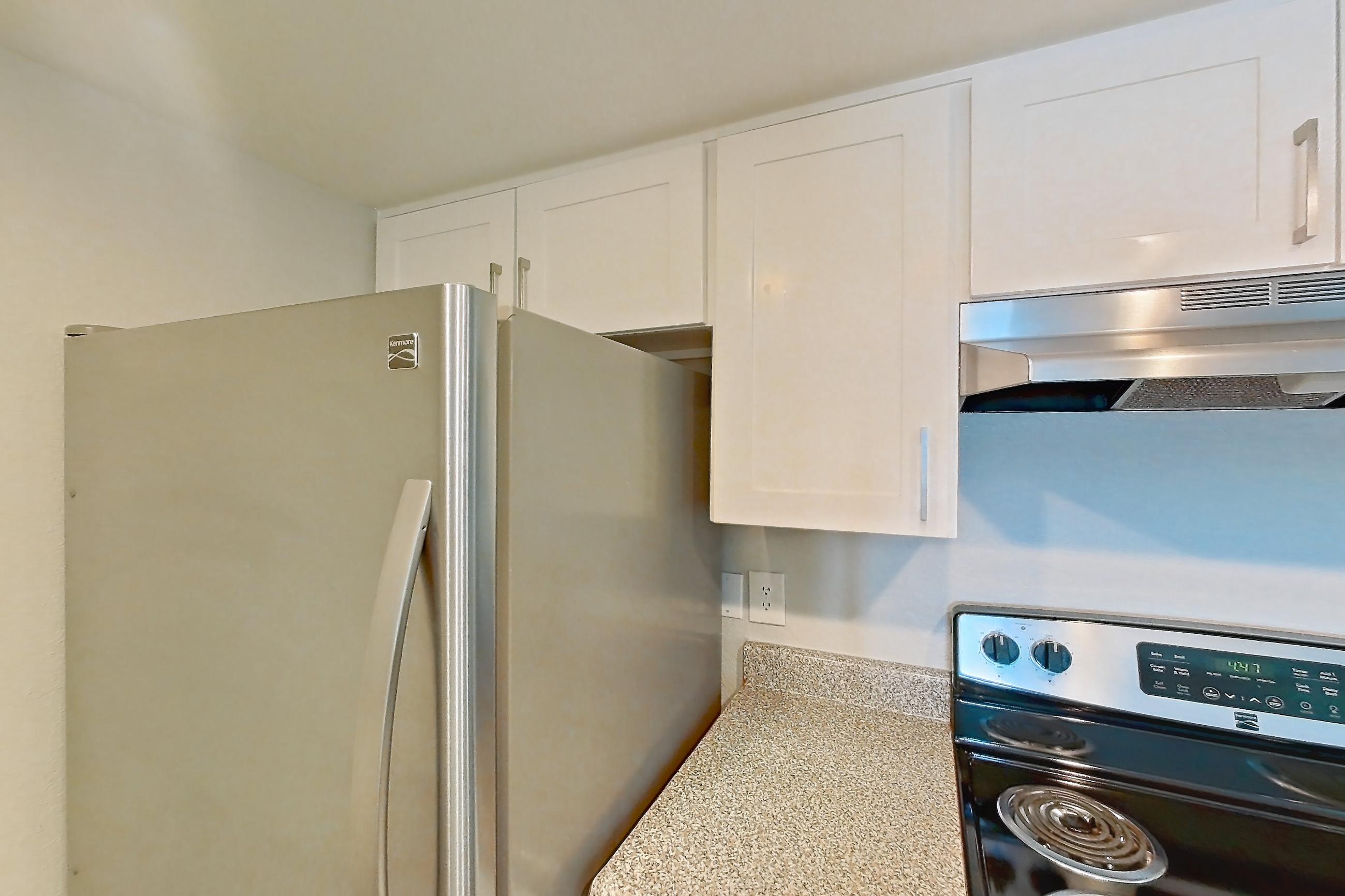 Kitchen with dishwasher, electric range, light countertops, light stone countertops, light wood-finish flooring, oven/range, range hood, refrigerator, and stainless steel appliances, Apartment 23 at Avana Rancho Cucamonga
