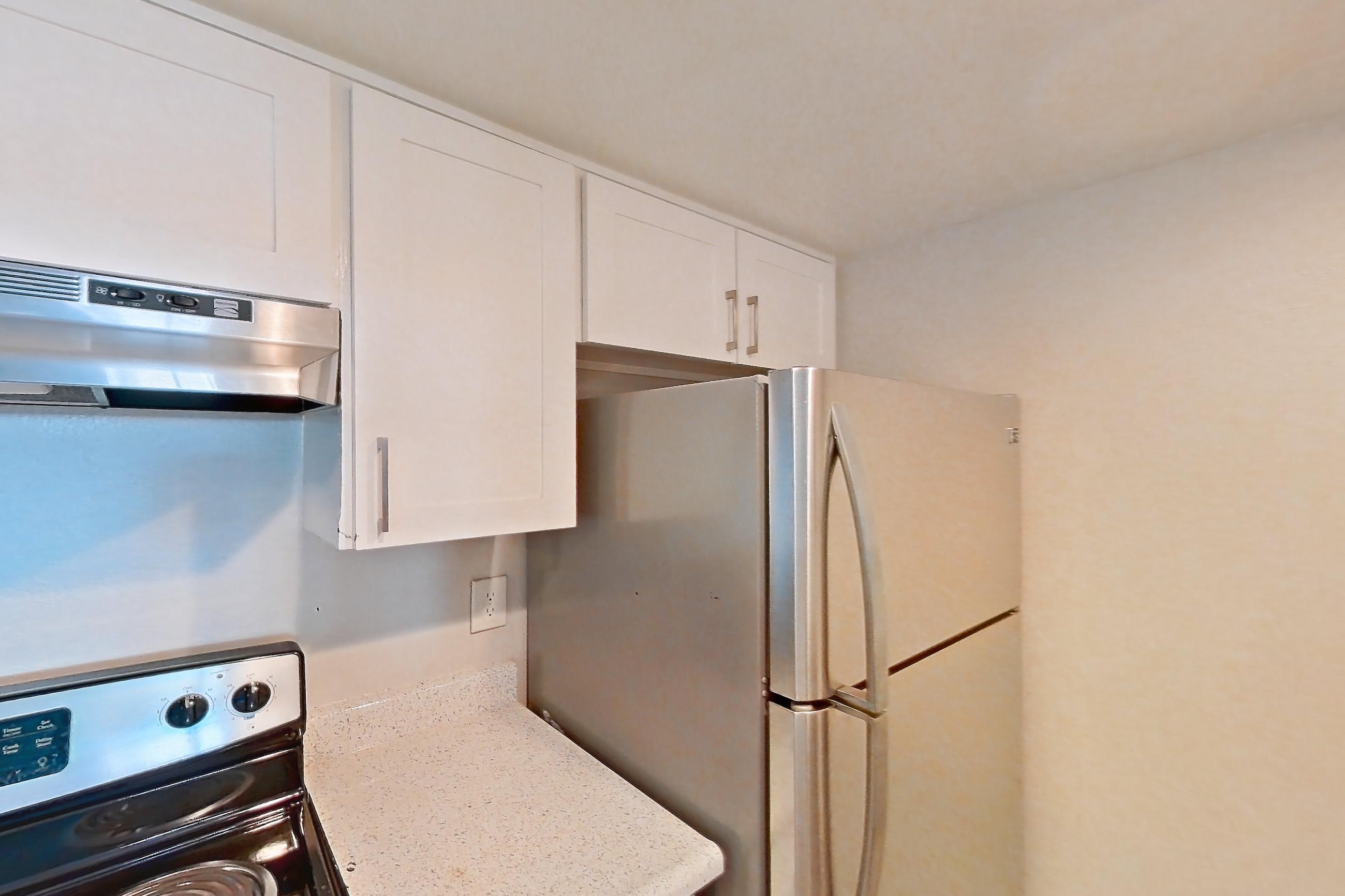 Kitchen with black appliances, electric range, light countertops, light stone countertops, light wood-finish flooring, oven/range, range hood, refrigerator, stainless steel appliances, and white appliances, Apartment 16 at Avana Rancho Cucamonga
