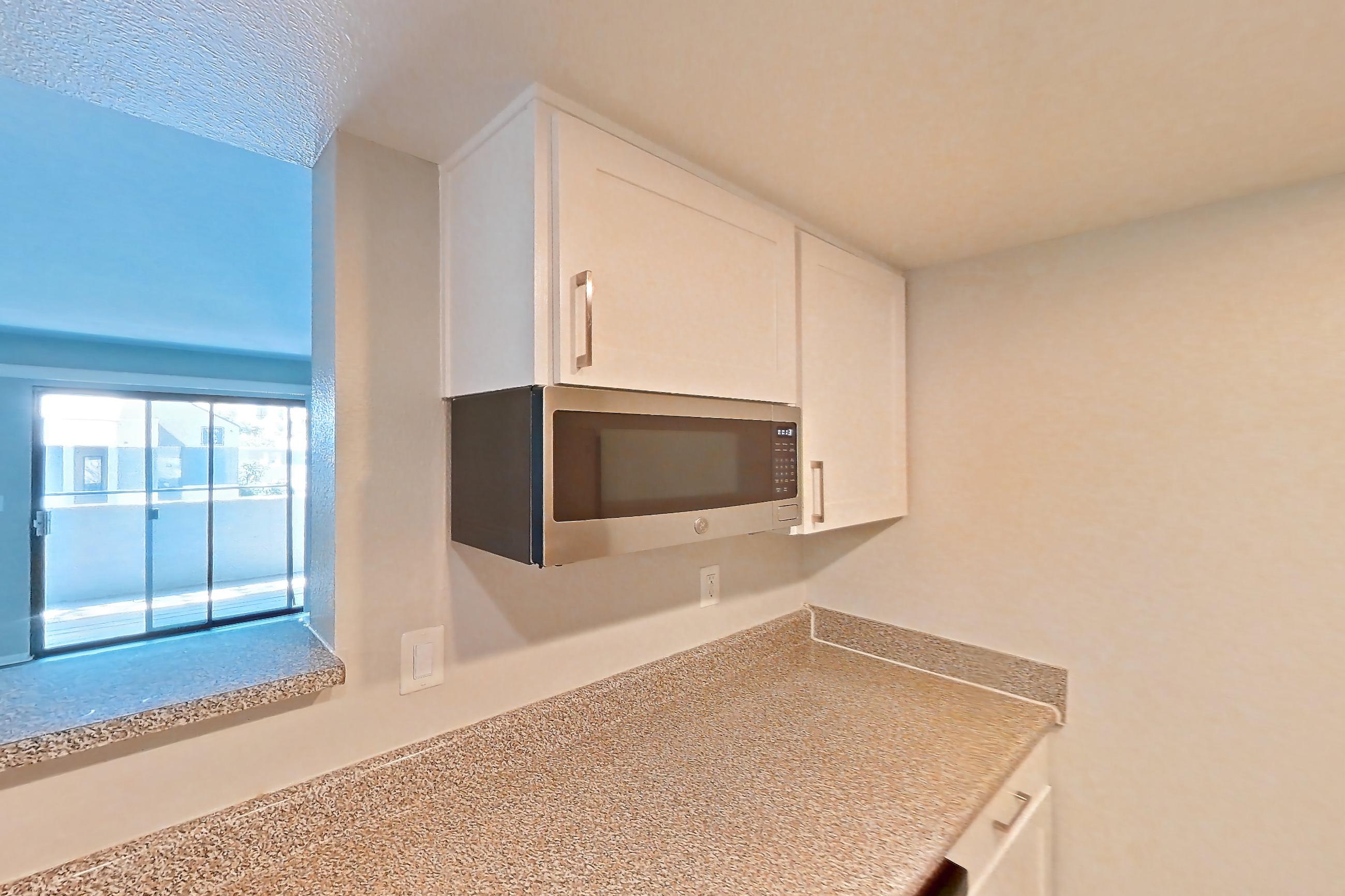 Kitchen with dishwasher, electric range, light countertops, light stone countertops, light wood-finish flooring, microwave, oven/range, and stainless steel appliances, Apartment 19 at Avana Rancho Cucamonga