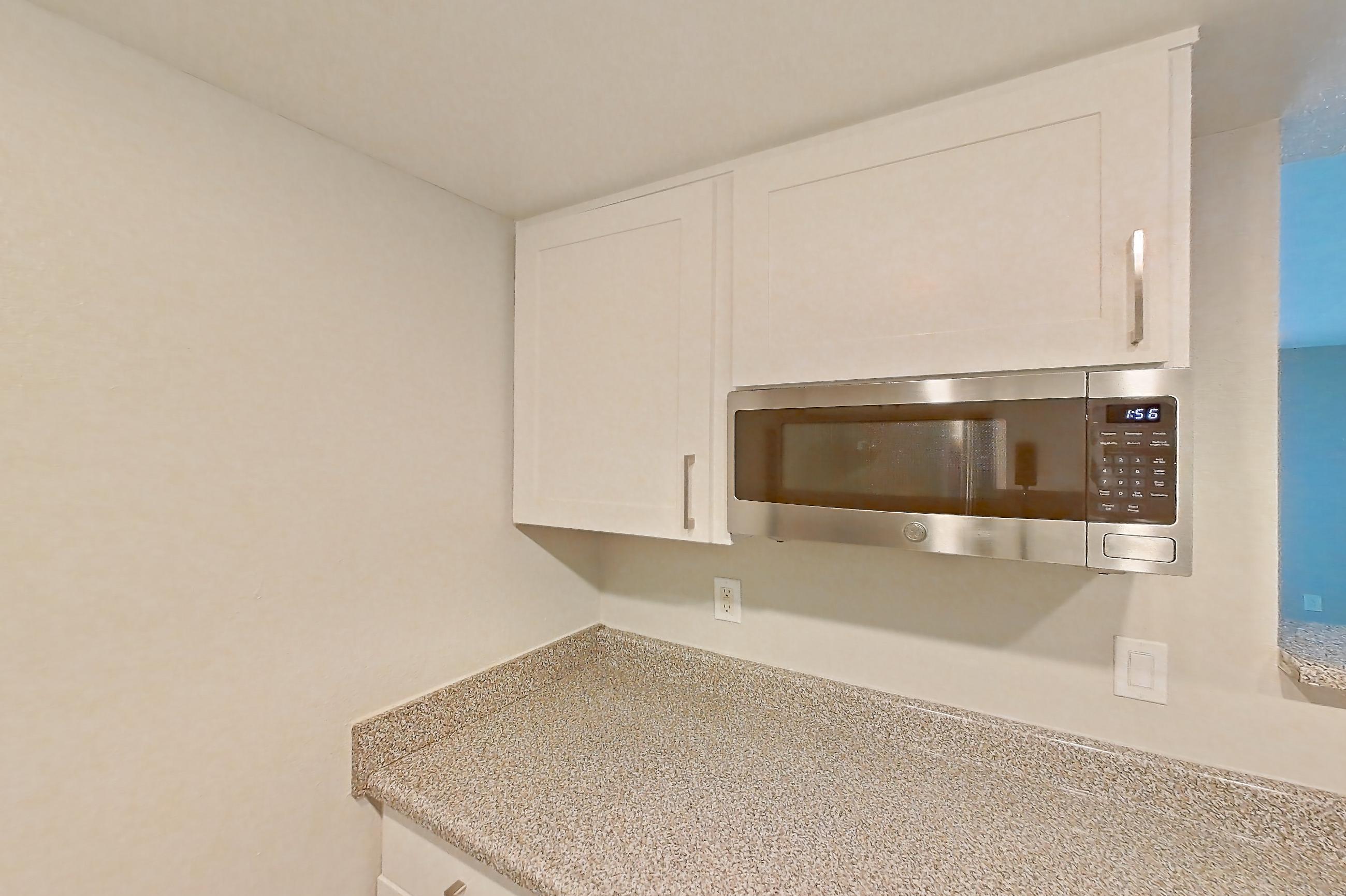 Kitchen with dishwasher, light stone countertops, light wood-finish flooring, microwave, refrigerator, and stainless steel appliances, Apartment 09 at Avana Rancho Cucamonga