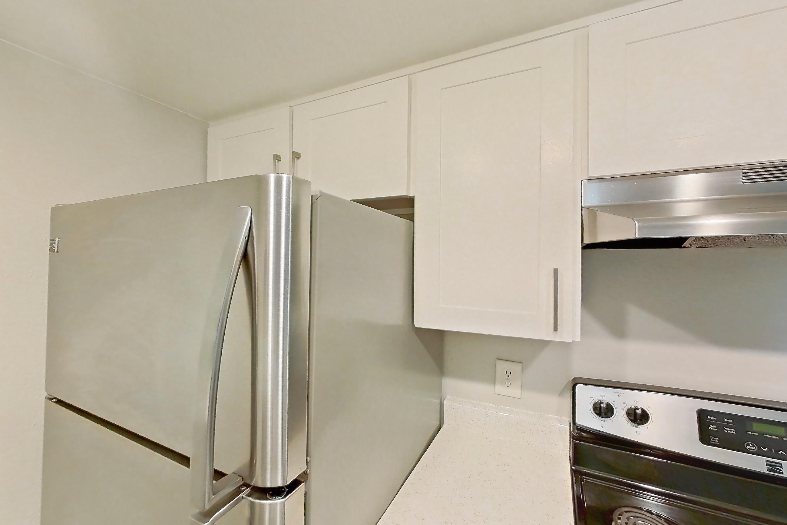 Kitchen with dishwasher, electric range, light countertops, light wood-finish flooring, oven/range, range hood, refrigerator, and stainless steel appliances, Apartment 23 at Avana Rancho Cucamonga