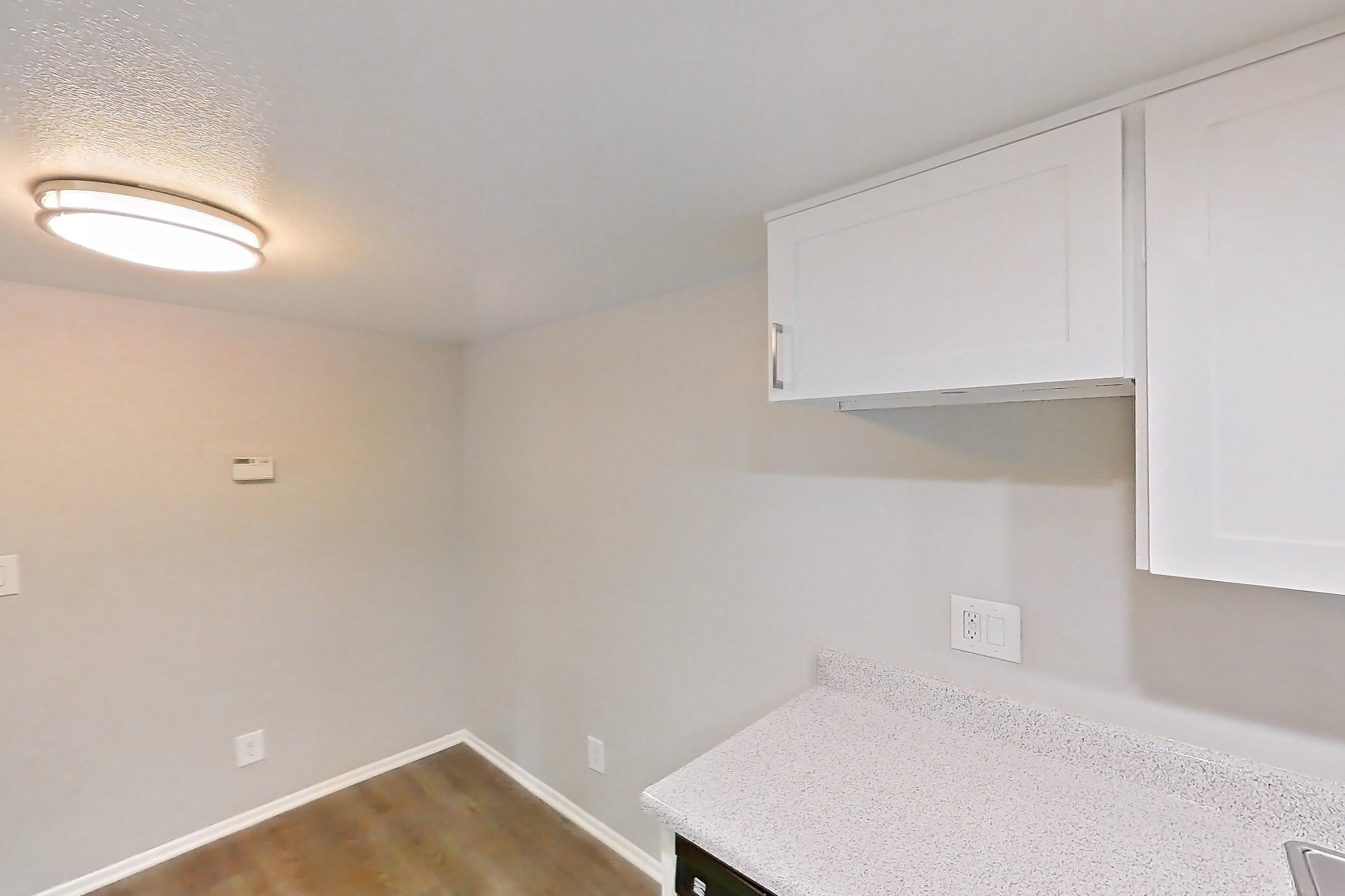 Kitchen with black appliances, dark wood-finish flooring, dishwasher, electric range, light countertops, light stone countertops, light wood-finish flooring, microwave, oven/range, and stainless steel appliances, Apartment 06 at Avana Rancho Cucamonga