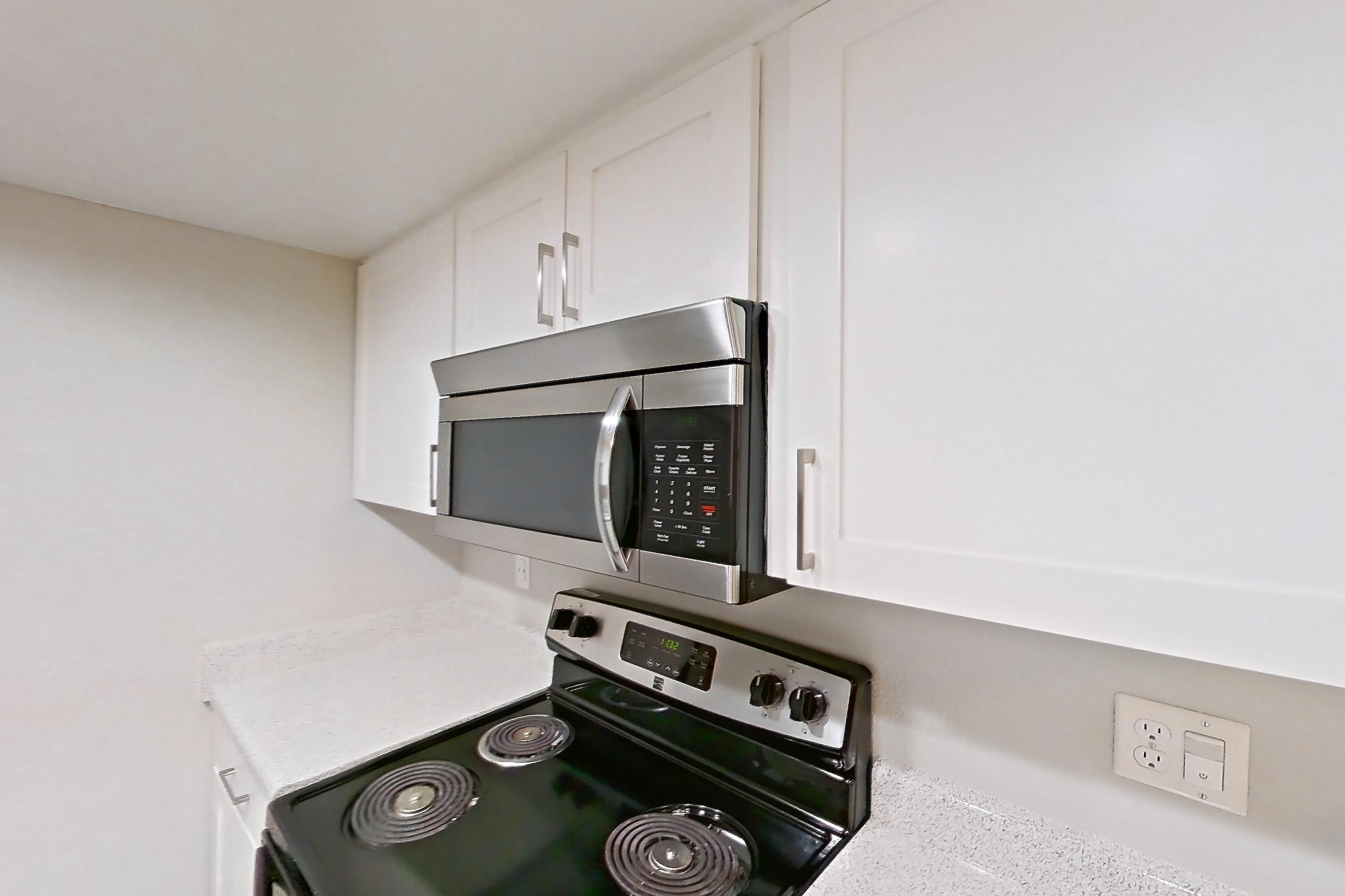 Kitchen with black appliances, dark wood-finish flooring, dishwasher, electric range, light countertops, light stone countertops, light wood-finish flooring, microwave, oven/range, and stainless steel appliances, Apartment 06 at Avana Rancho Cucamonga