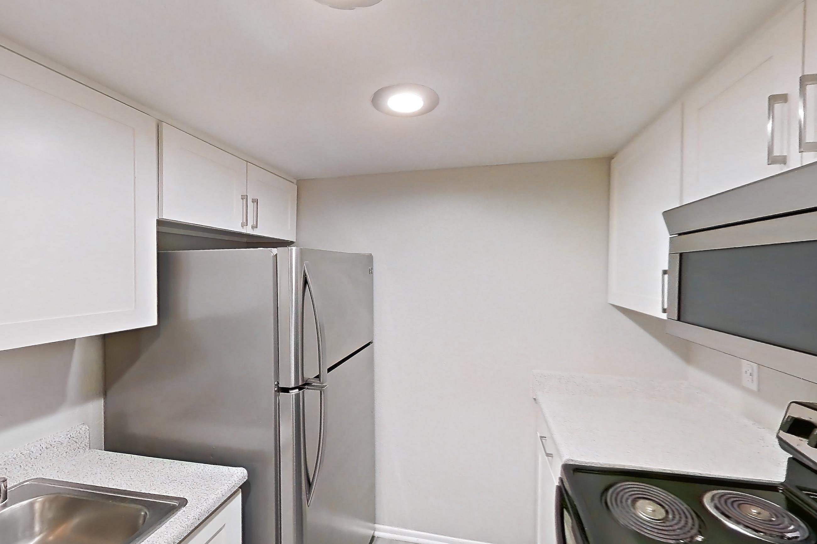 Kitchen with black appliances, dark wood-finish flooring, dishwasher, electric range, light countertops, light stone countertops, light wood-finish flooring, microwave, oven/range, and stainless steel appliances, Apartment 06 at Avana Rancho Cucamonga