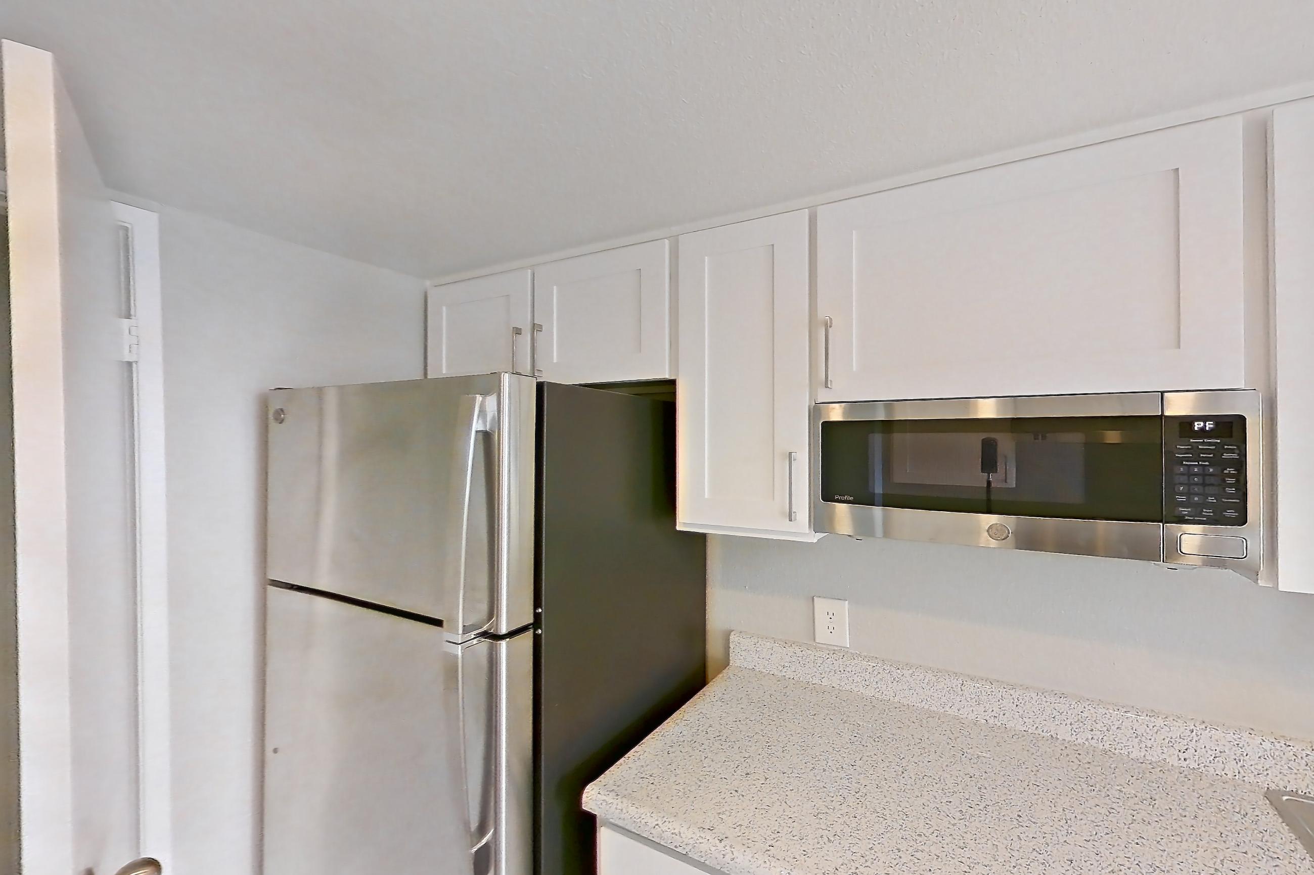 Kitchen with dark wood-finish flooring, dishwasher, electric range, light countertops, light stone countertops, light wood-finish flooring, oven/range, refrigerator, and stainless steel appliances, Apartment 11 at Avana Rancho Cucamonga