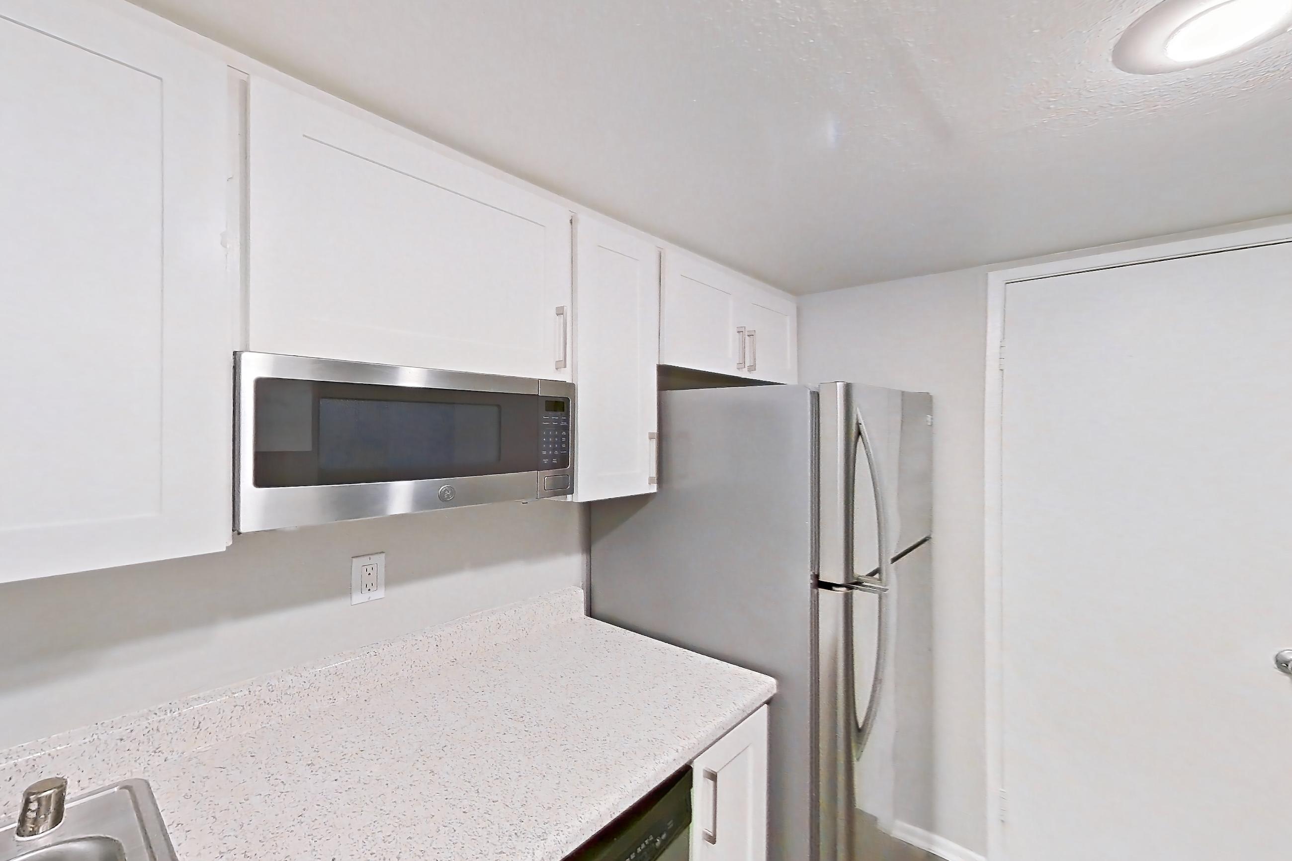 Kitchen with dishwasher, electric range, light countertops, light stone countertops, light wood-finish flooring, microwave, oven/range, refrigerator, and stainless steel appliances, Apartment 01 at Avana Rancho Cucamonga