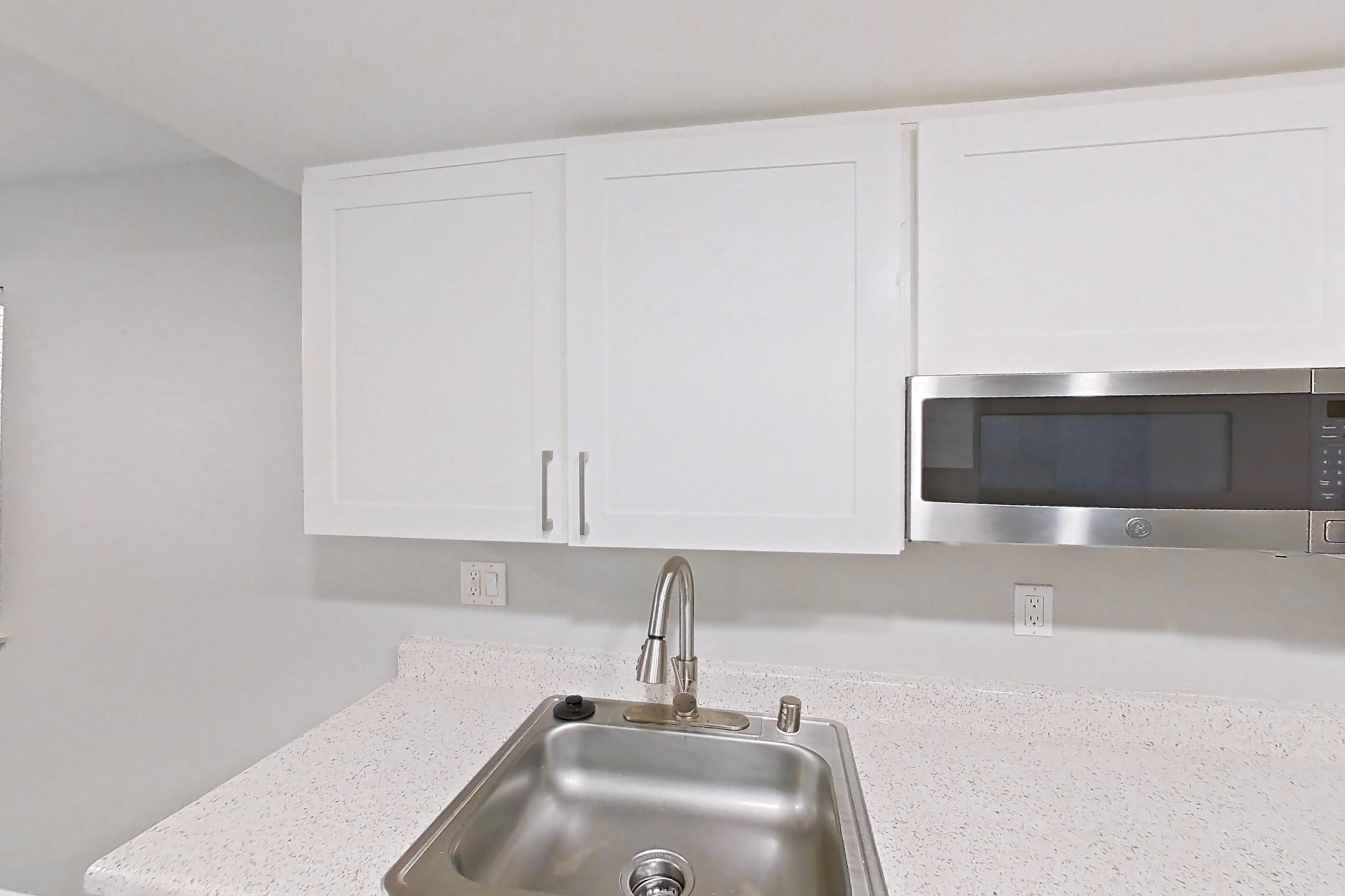 Kitchen with dishwasher, electric range, light countertops, light stone countertops, light wood-finish flooring, microwave, oven/range, refrigerator, and stainless steel appliances, Apartment 01 at Avana Rancho Cucamonga
