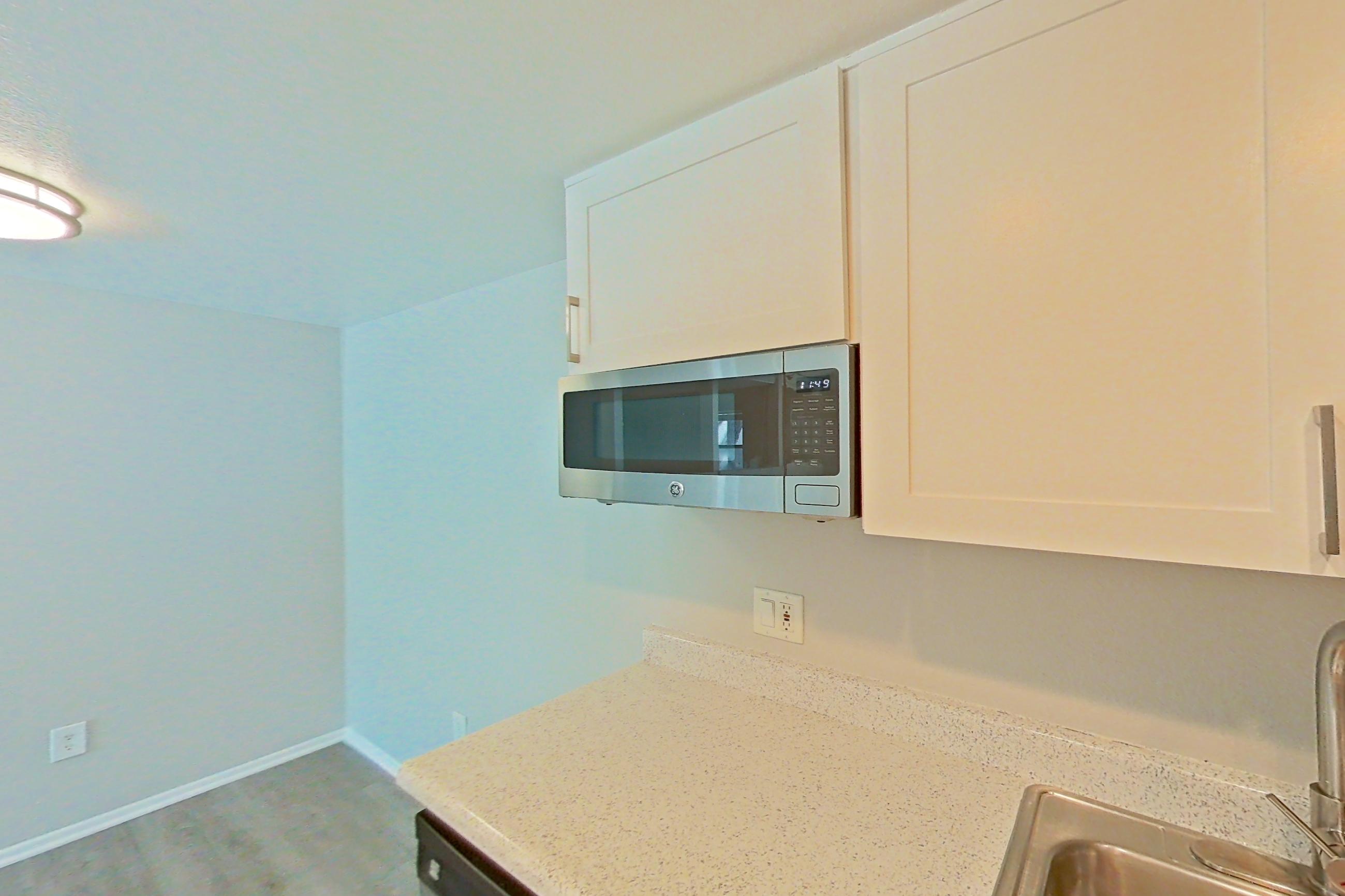 Kitchen with dark countertops, dishwasher, electric range, light stone countertops, light wood-finish flooring, oven/range, range hood, and stainless steel appliances, Apartment 10 at Avana Rancho Cucamonga