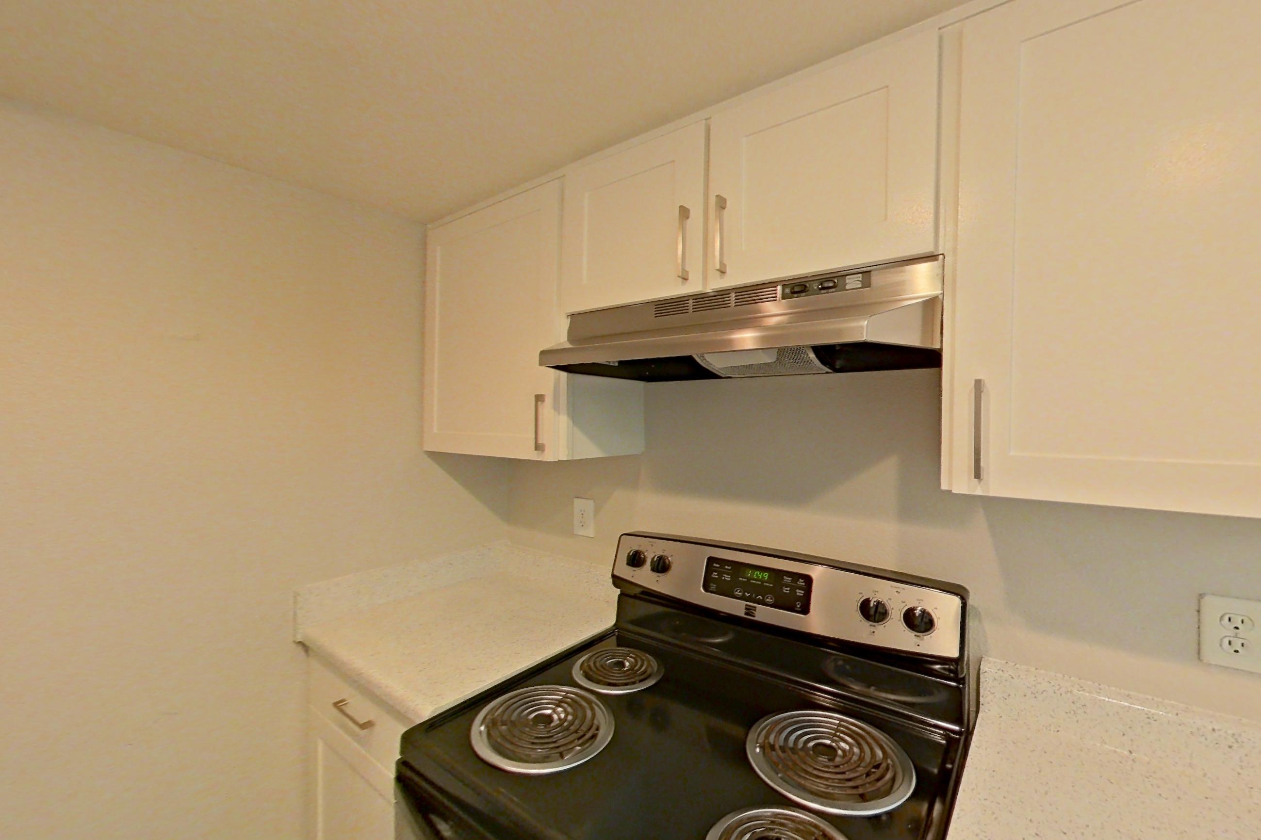 Kitchen with dark countertops, dishwasher, electric range, light stone countertops, light wood-finish flooring, oven/range, range hood, and stainless steel appliances, Apartment 10 at Avana Rancho Cucamonga