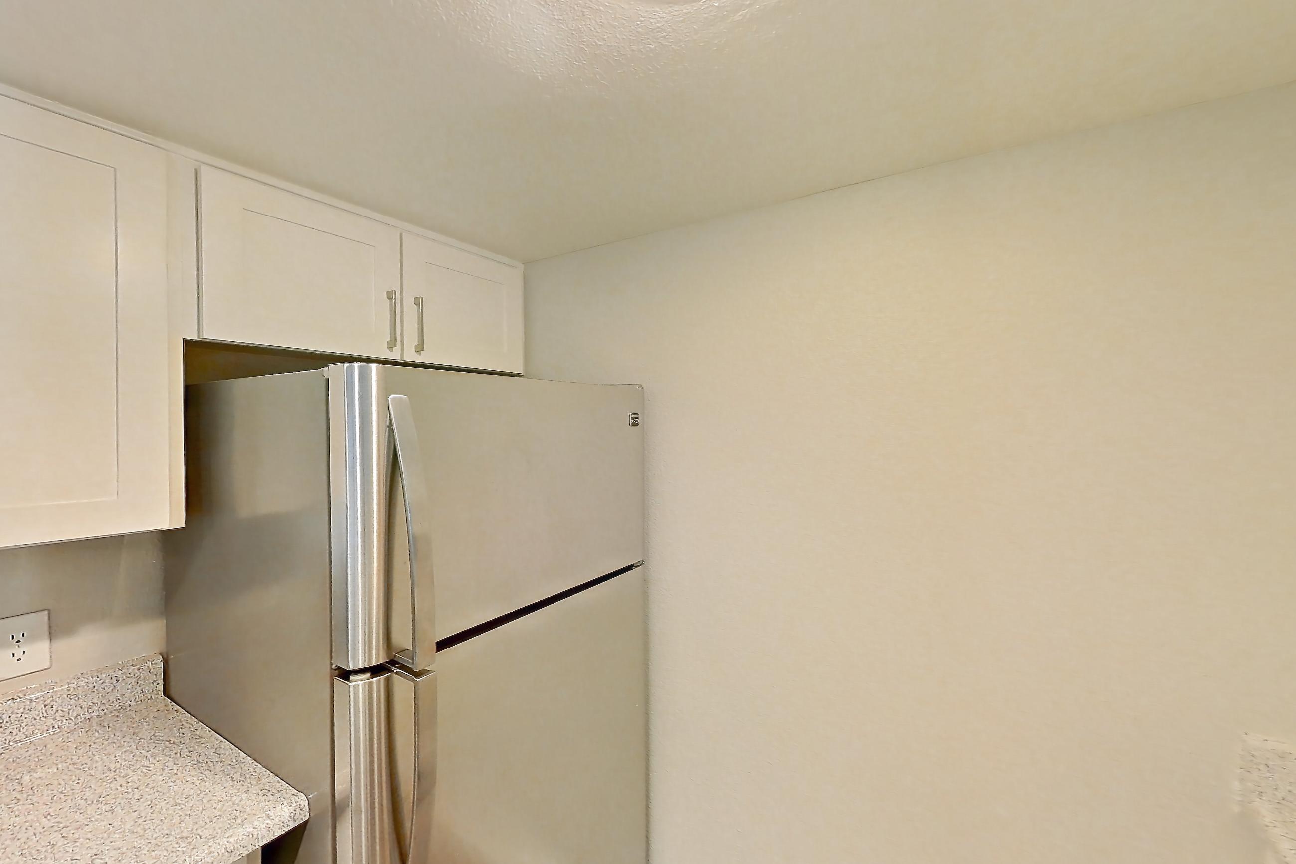 Kitchen with dishwasher, electric range, in-unit laundry, light countertops, light stone countertops, light wood-finish flooring, microwave, oven/range, refrigerator, and stainless steel appliances, Apartment 05 at Avana Rancho Cucamonga