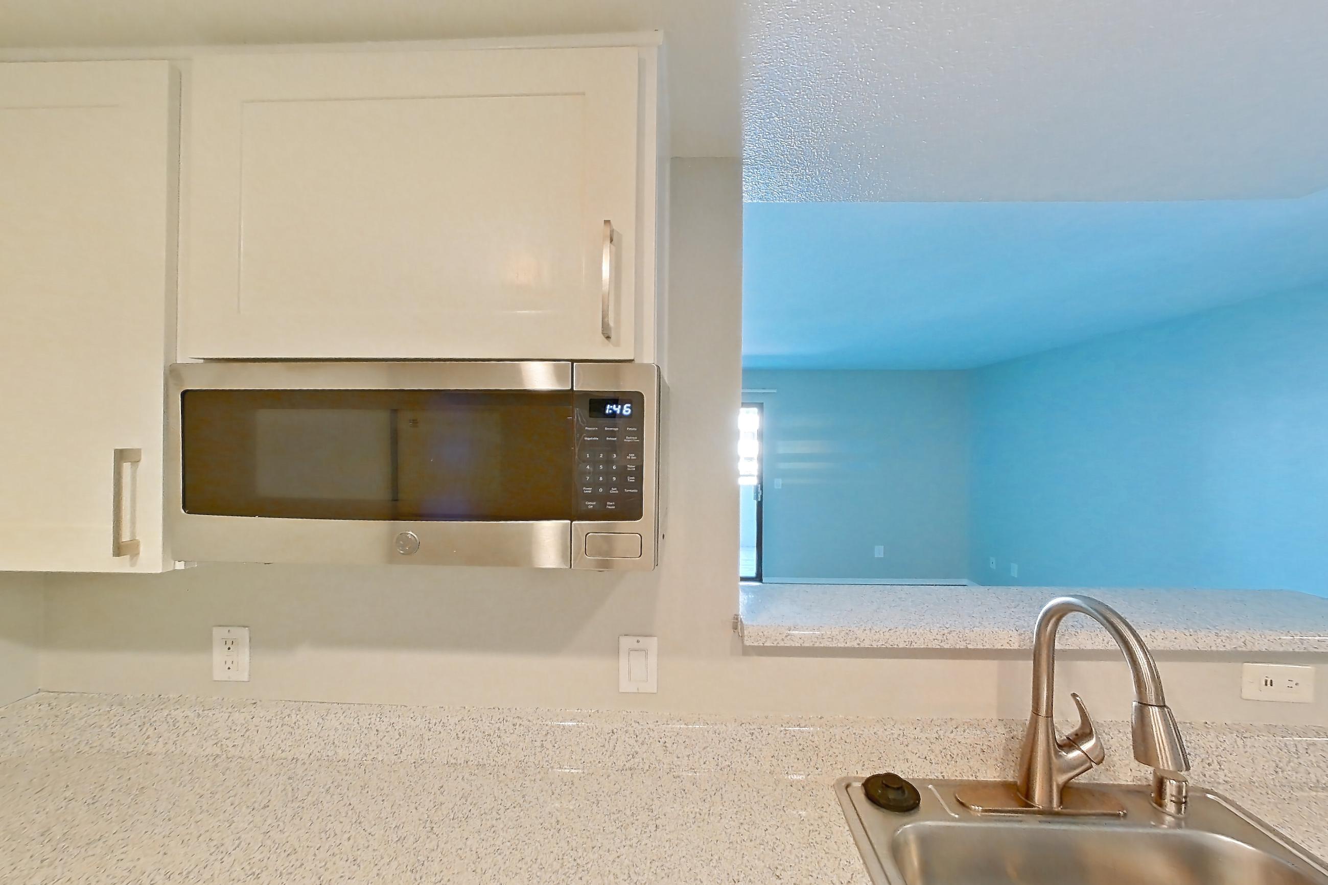 Kitchen with dishwasher, electric range, in-unit laundry, light countertops, light stone countertops, light wood-finish flooring, microwave, oven/range, refrigerator, and stainless steel appliances, Apartment 05 at Avana Rancho Cucamonga