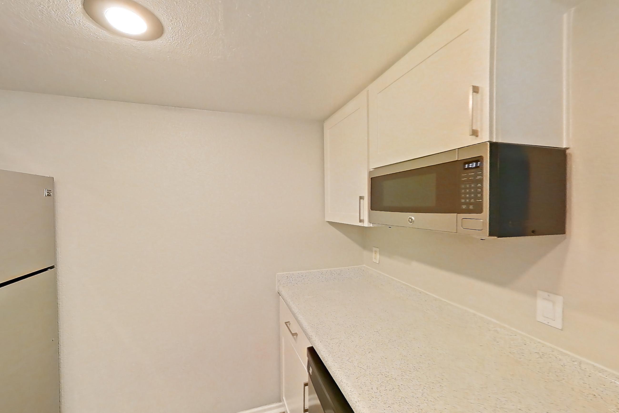 Kitchen with dark wood-finish flooring, dishwasher, electric range, light countertops, light stone countertops, light wood-finish flooring, microwave, oven/range, and stainless steel appliances, Apartment 01 at Avana Rancho Cucamonga