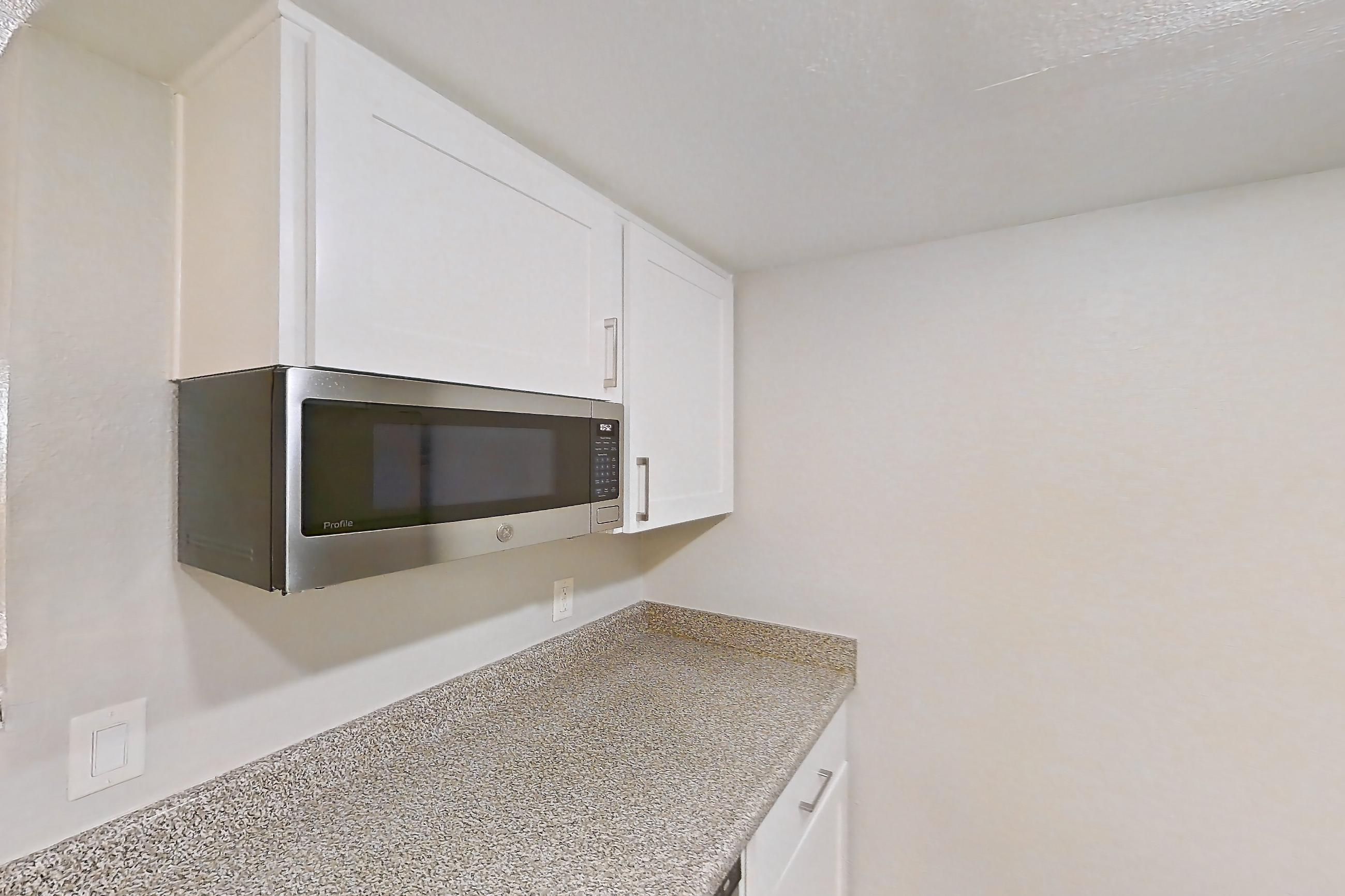 Kitchen with dishwasher, electric range, light stone countertops, light wood-finish flooring, microwave, oven/range, refrigerator, and stainless steel appliances, Apartment 22 at Avana Rancho Cucamonga
