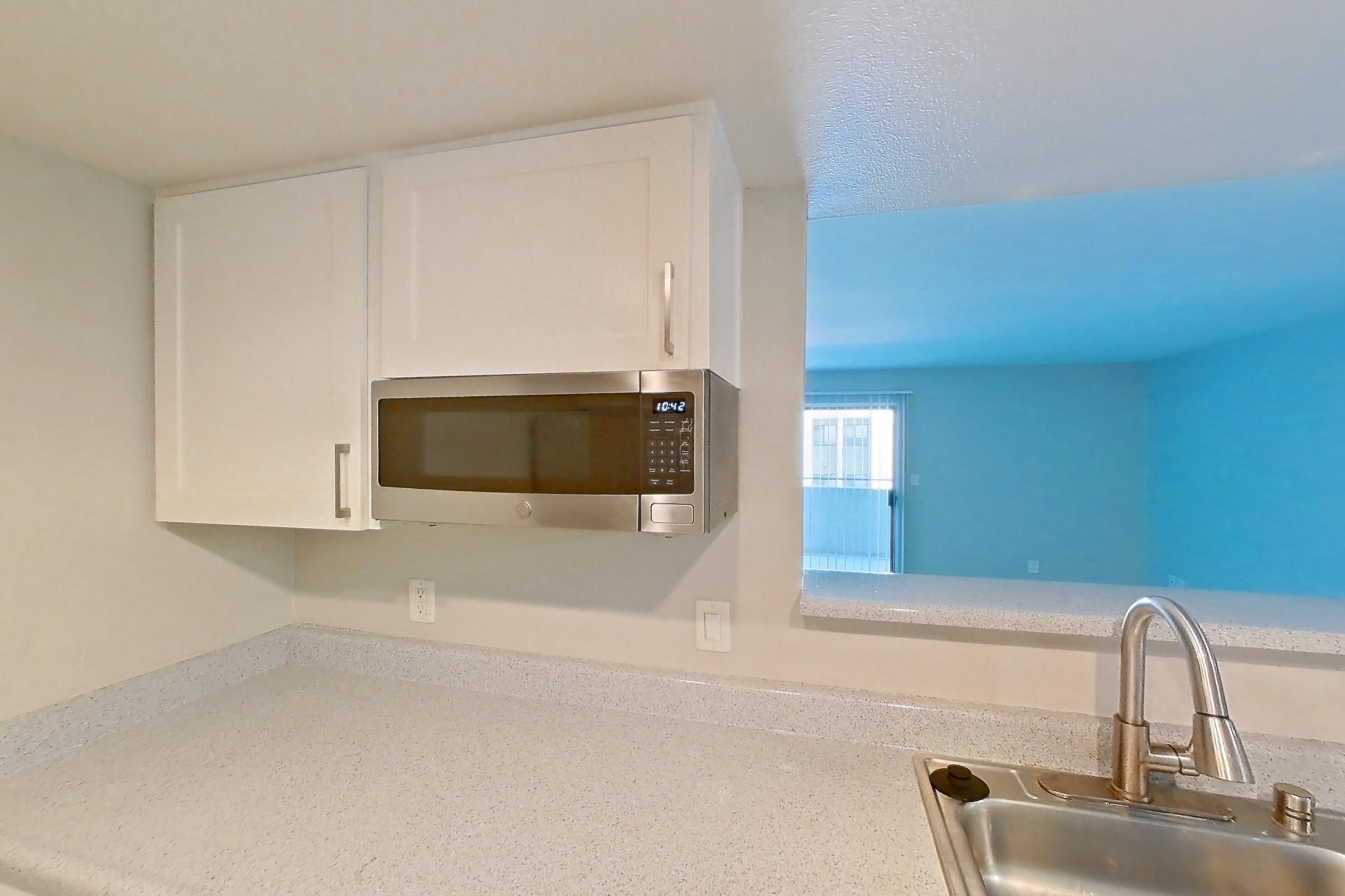 Kitchen with dishwasher, light countertops, light stone countertops, light wood-finish flooring, oven/range, refrigerator, stainless steel appliances, and white appliances, Apartment 05 at Avana Rancho Cucamonga