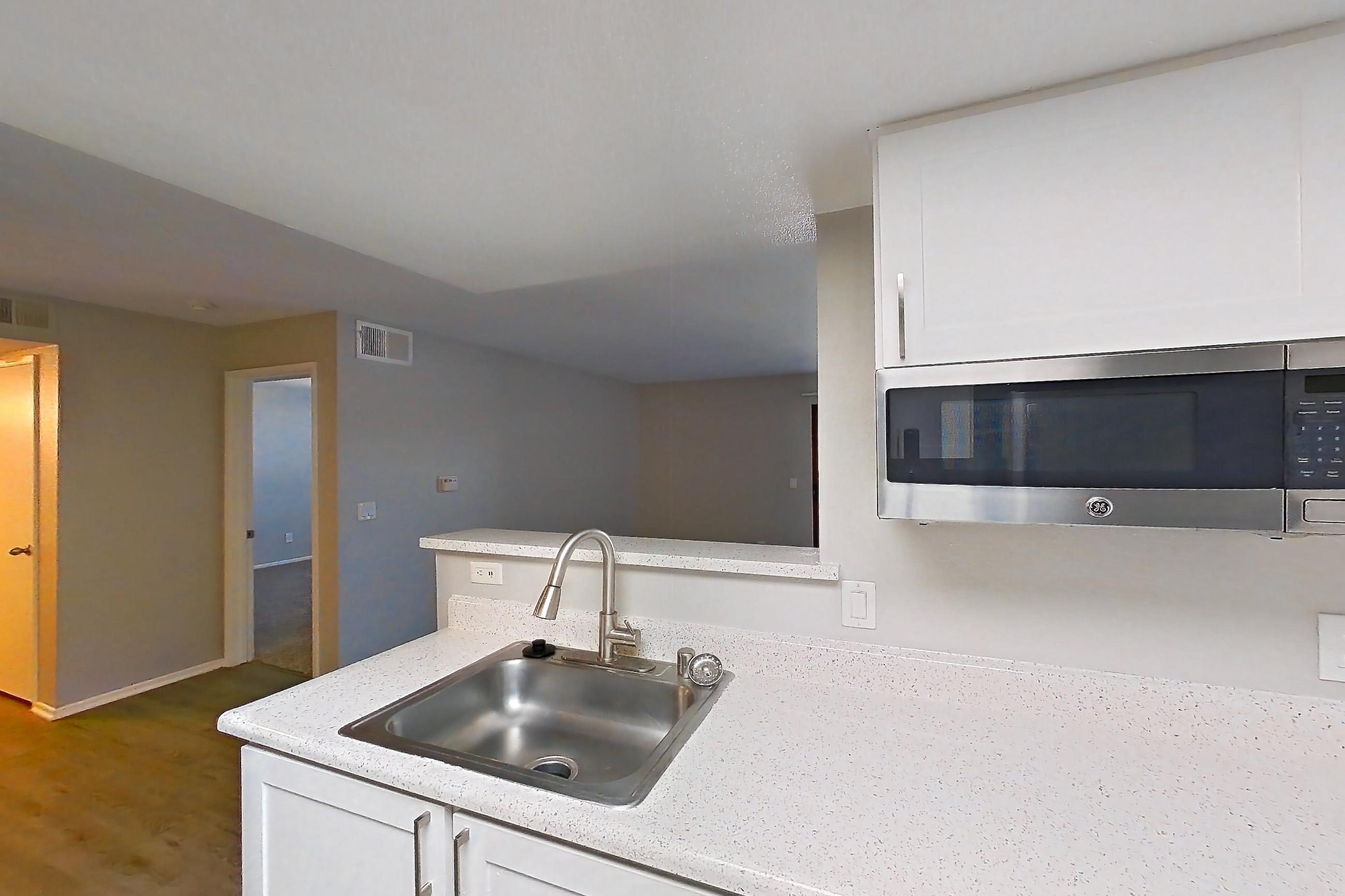 Kitchen with dishwasher, electric range, light countertops, light stone countertops, light wood-finish flooring, oven/range, range hood, refrigerator, stainless steel appliances, and white appliances, Apartment 11 at Avana Rancho Cucamonga