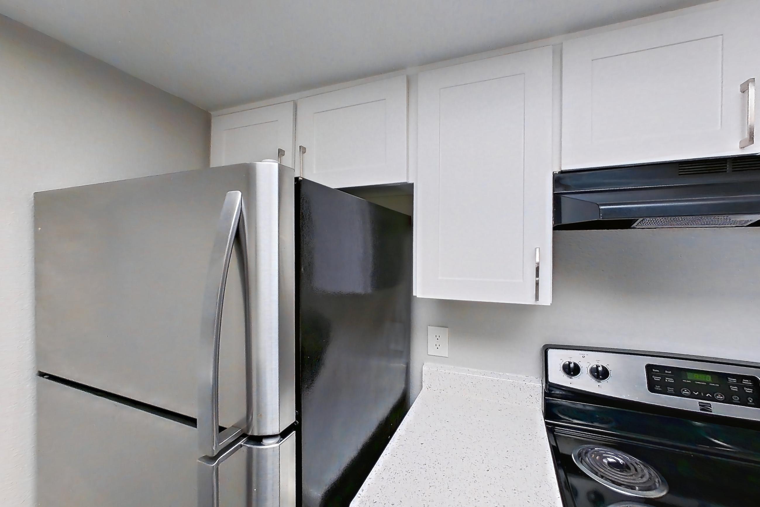 Kitchen with dishwasher, electric range, light countertops, light stone countertops, light wood-finish flooring, oven/range, range hood, refrigerator, stainless steel appliances, and white appliances, Apartment 11 at Avana Rancho Cucamonga