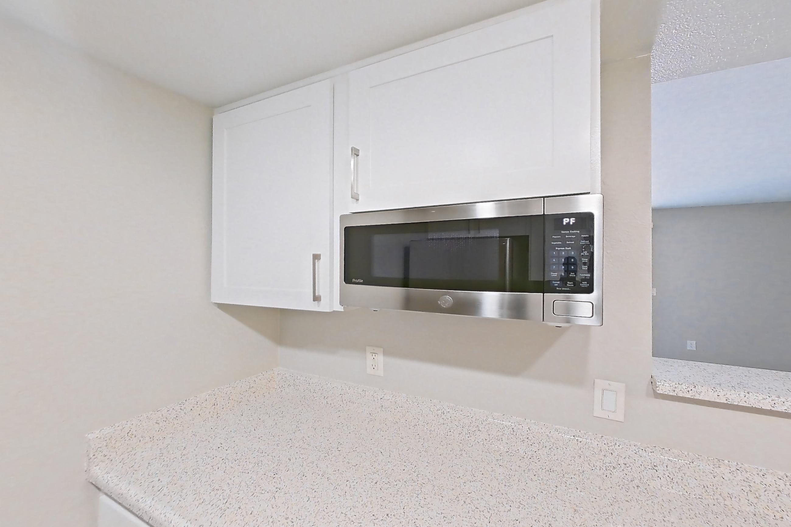 Kitchen with dishwasher, light countertops, light stone countertops, light wood-finish flooring, microwave, refrigerator, and stainless steel appliances, Apartment 12 at Avana Rancho Cucamonga