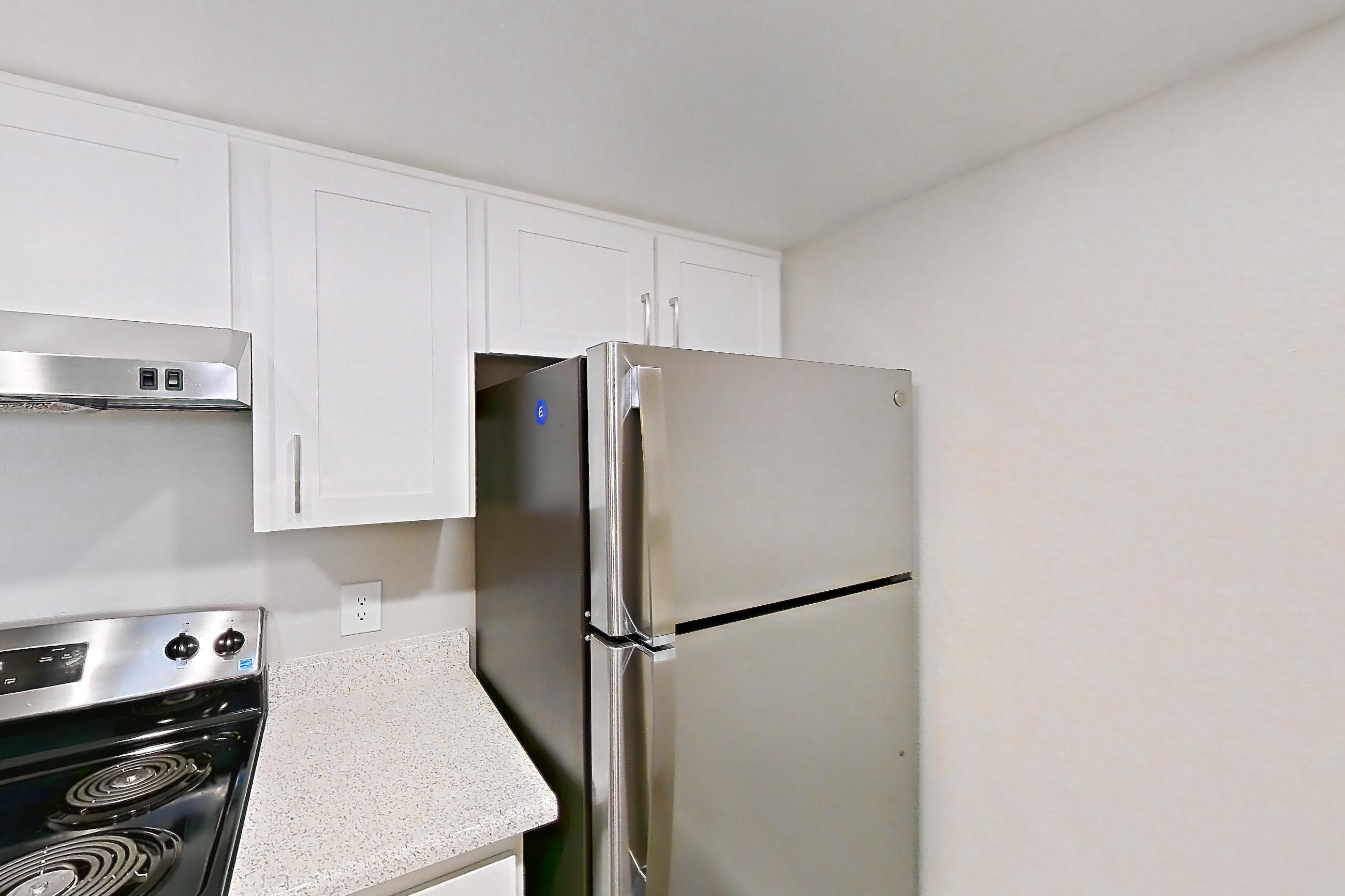 Kitchen with dishwasher, light countertops, light stone countertops, light wood-finish flooring, microwave, refrigerator, and stainless steel appliances, Apartment 12 at Avana Rancho Cucamonga
