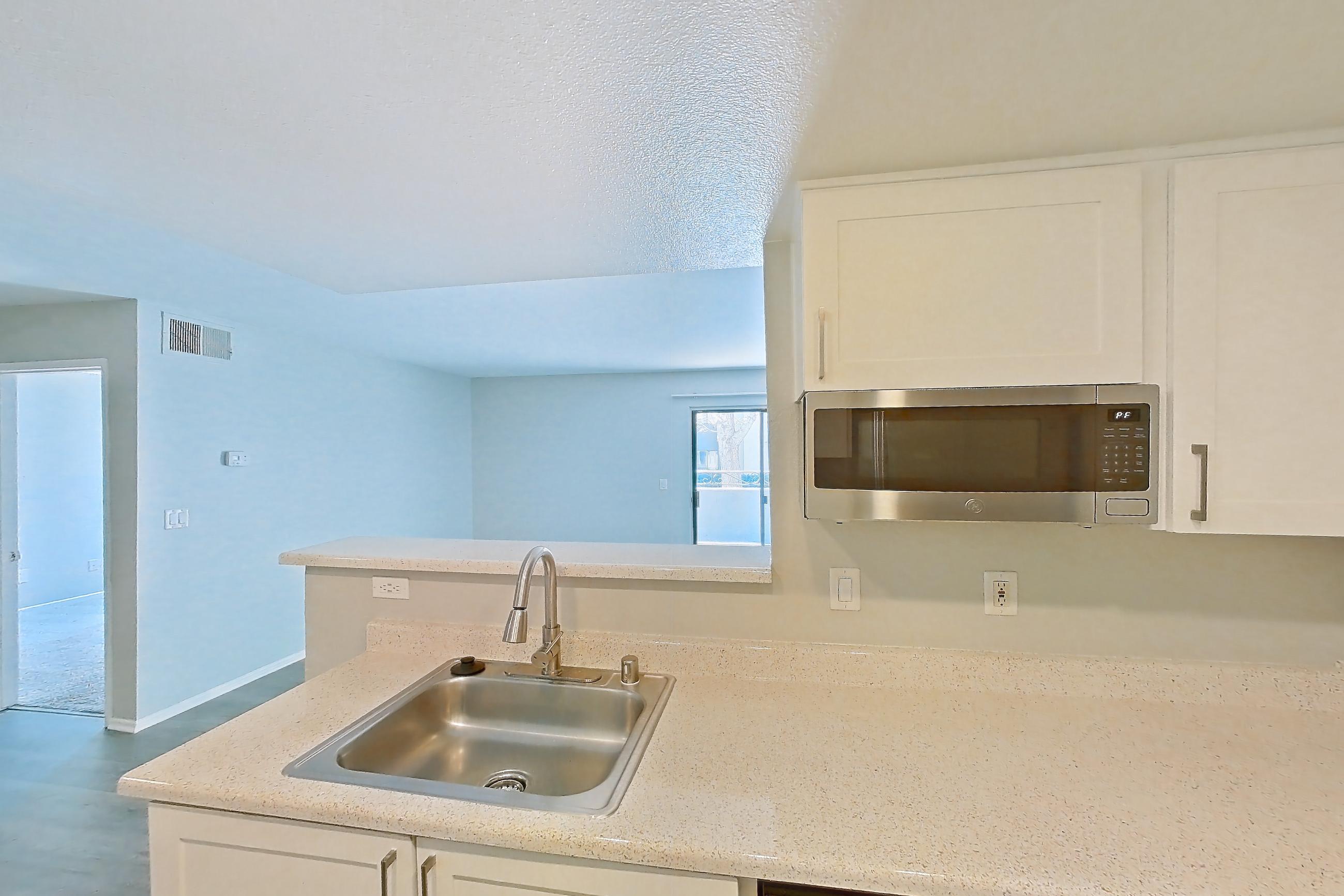Kitchen with dishwasher, electric range, in-unit laundry, light countertops, light stone countertops, light wood-finish flooring, oven/range, range hood, refrigerator, and stainless steel appliances, Apartment 14 at Avana Rancho Cucamonga