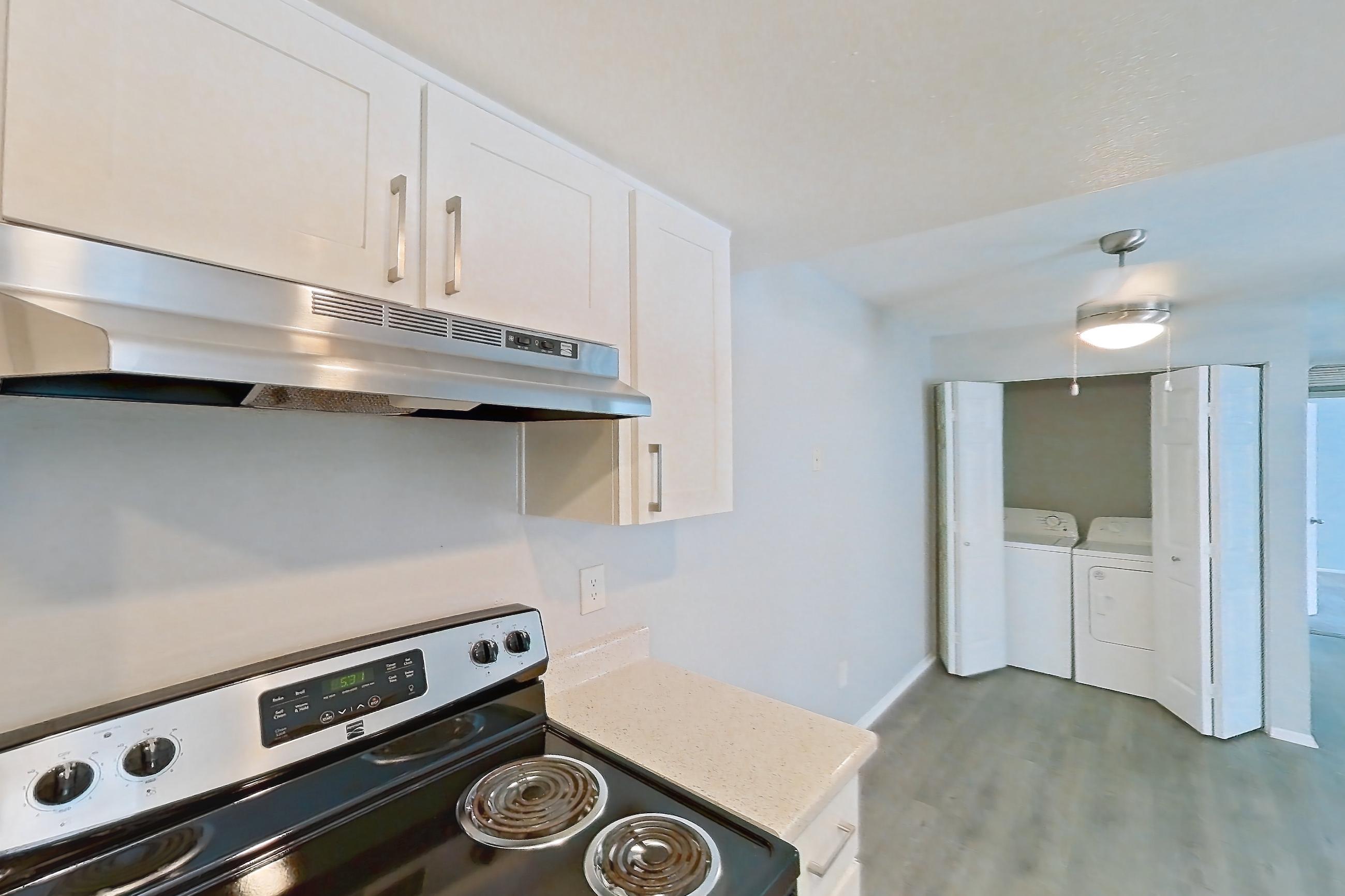Kitchen with dishwasher, electric range, in-unit laundry, light countertops, light stone countertops, light wood-finish flooring, oven/range, range hood, refrigerator, and stainless steel appliances, Apartment 14 at Avana Rancho Cucamonga