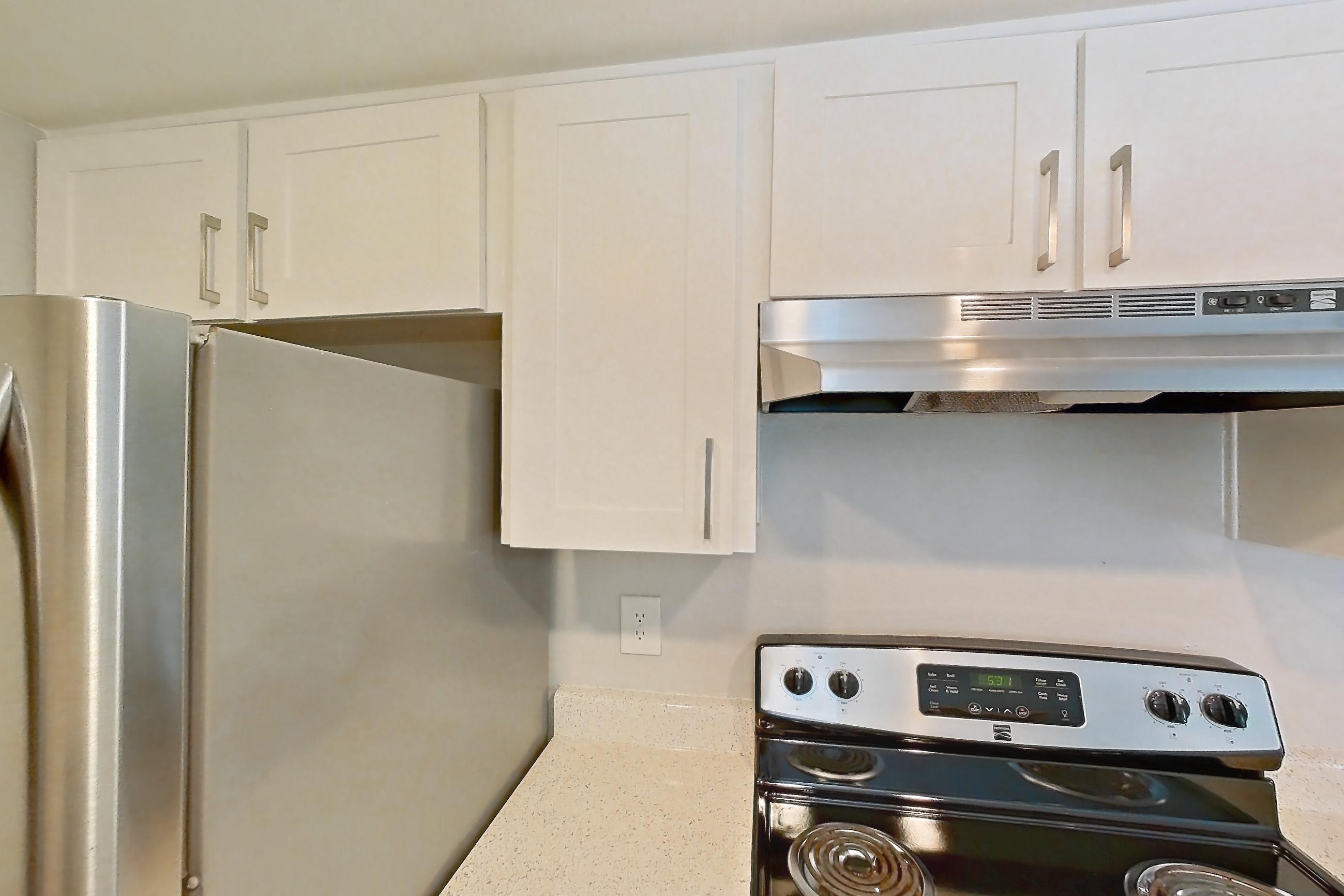 Kitchen with dishwasher, electric range, in-unit laundry, light countertops, light stone countertops, light wood-finish flooring, oven/range, range hood, refrigerator, and stainless steel appliances, Apartment 14 at Avana Rancho Cucamonga